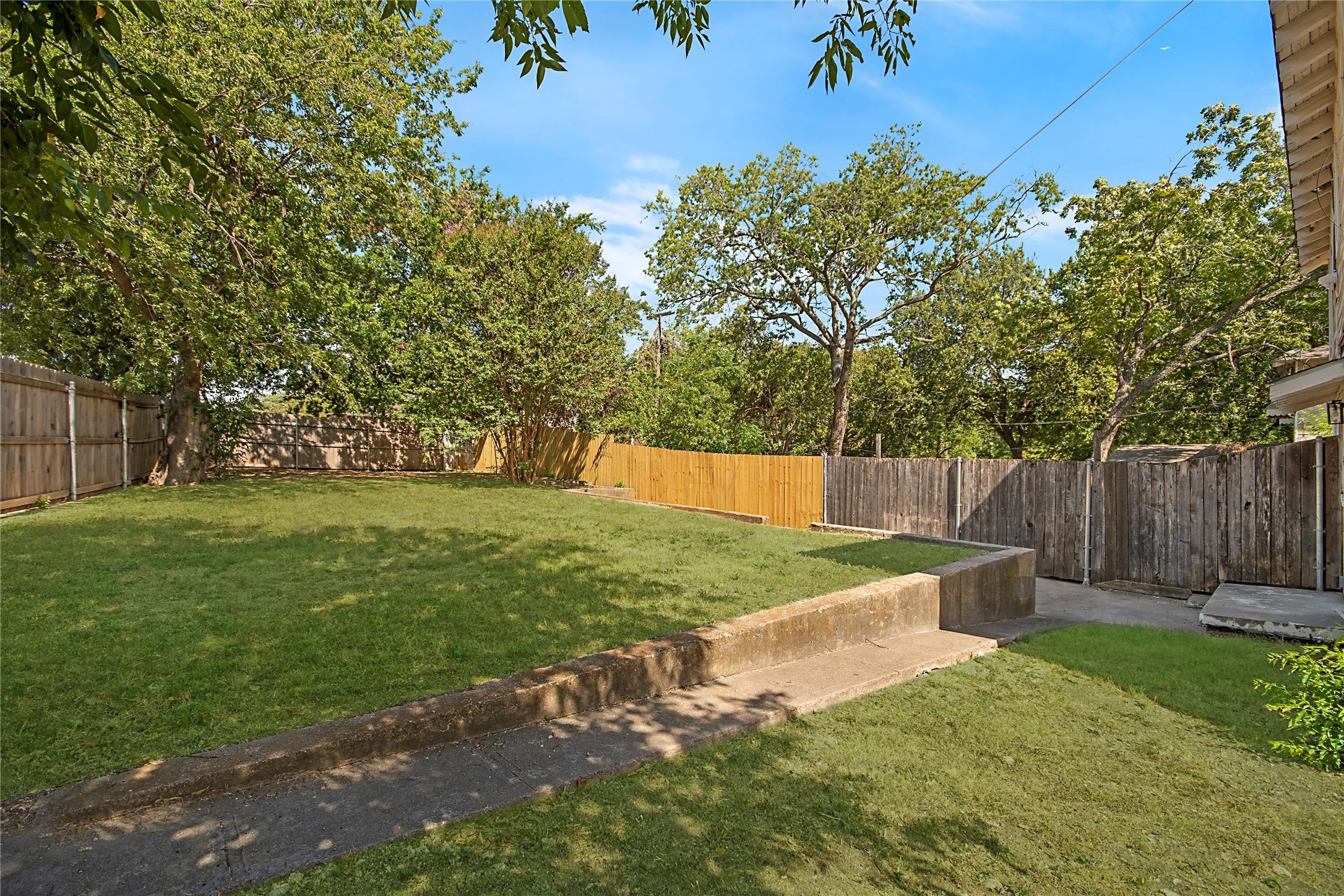 Expansive backyard featuring a manicured lawn, mature trees, and privacy fencing