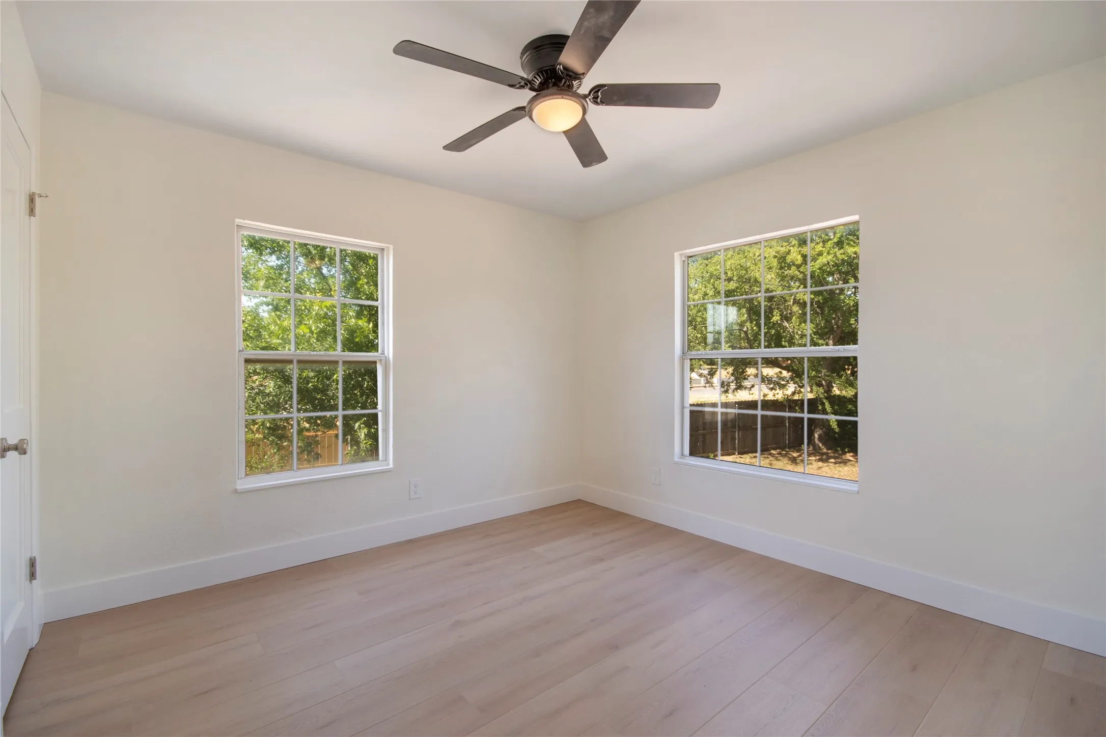 Neutral wall paint throughout, two large windows, wood-finish flooring, and a ceiling fan with integrated lighting