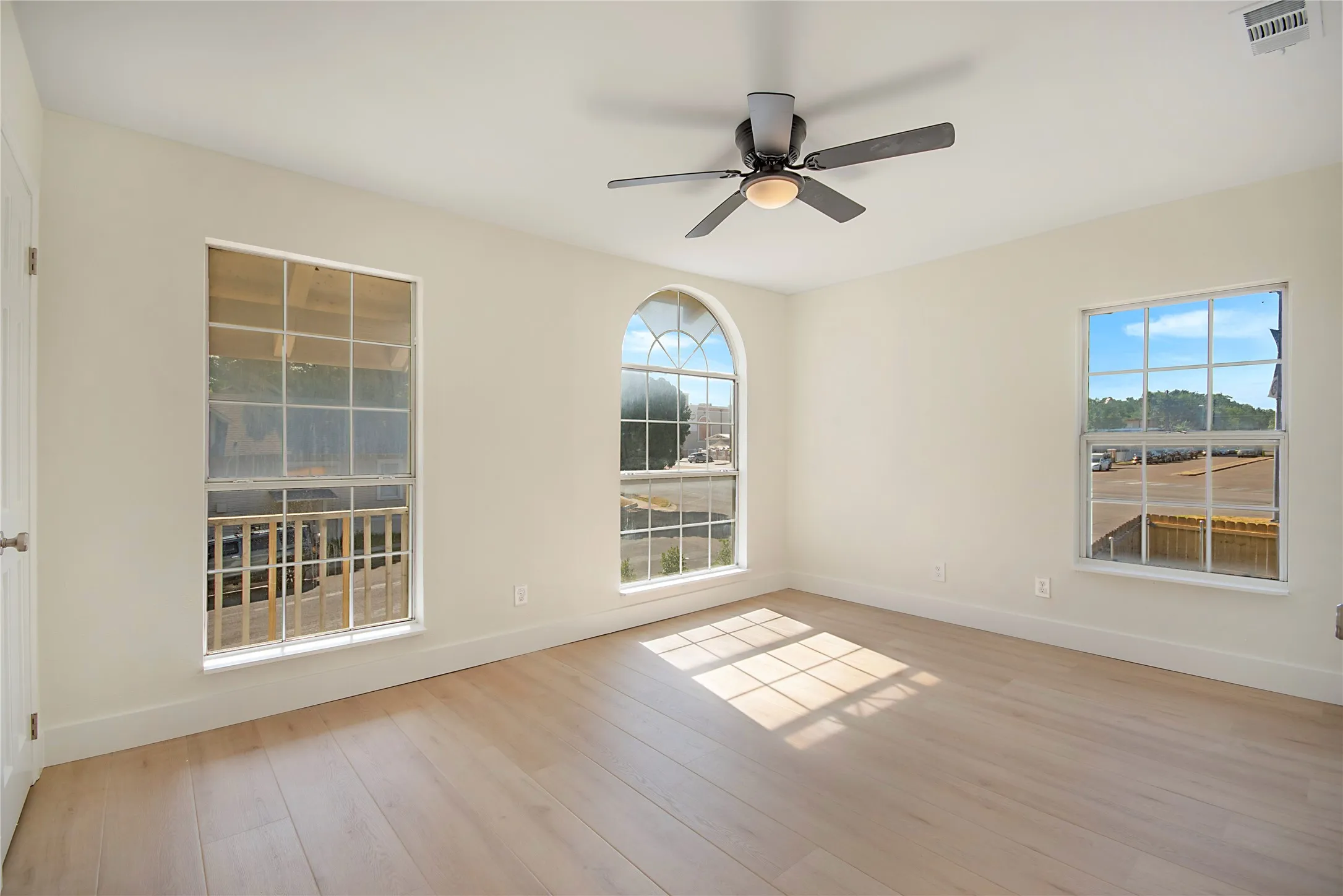 Light-toned wood-finish flooring, white walls, arched window, two rectangular windows, and a ceiling fan with integrated lighting