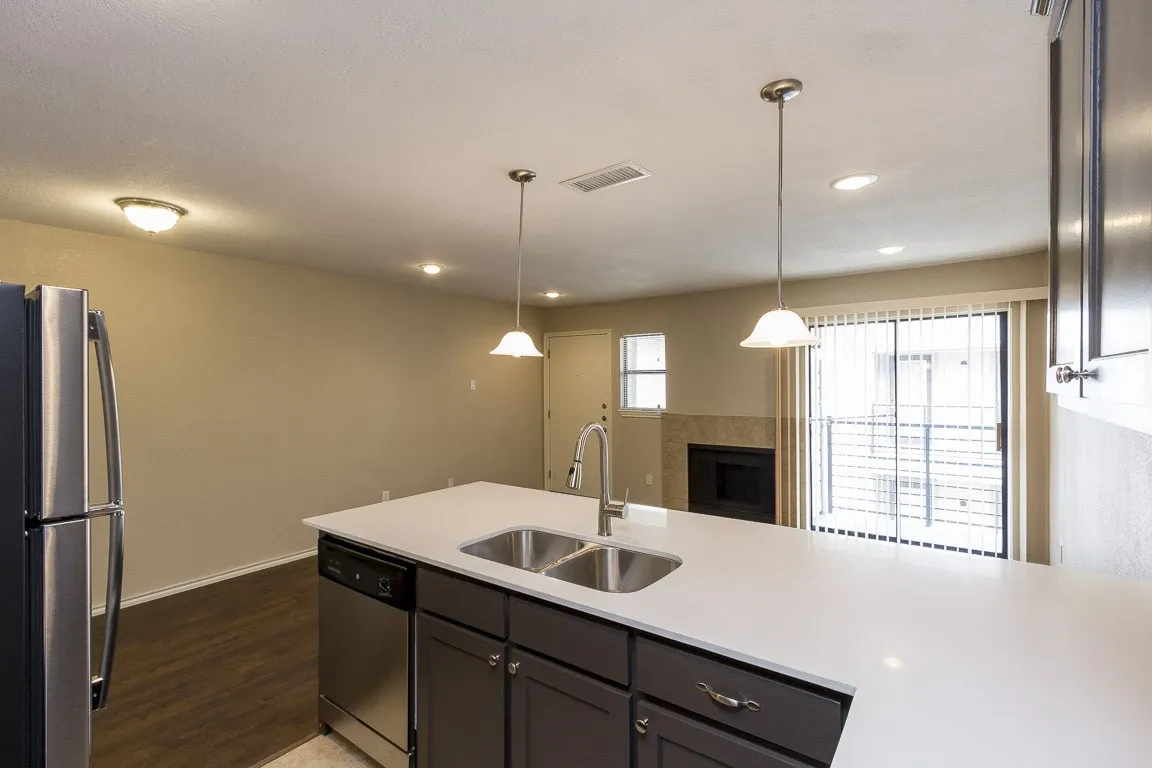 Kitchen island with dual pendant lighting, stainless steel sink, integrated dishwasher, and wood-finish flooring