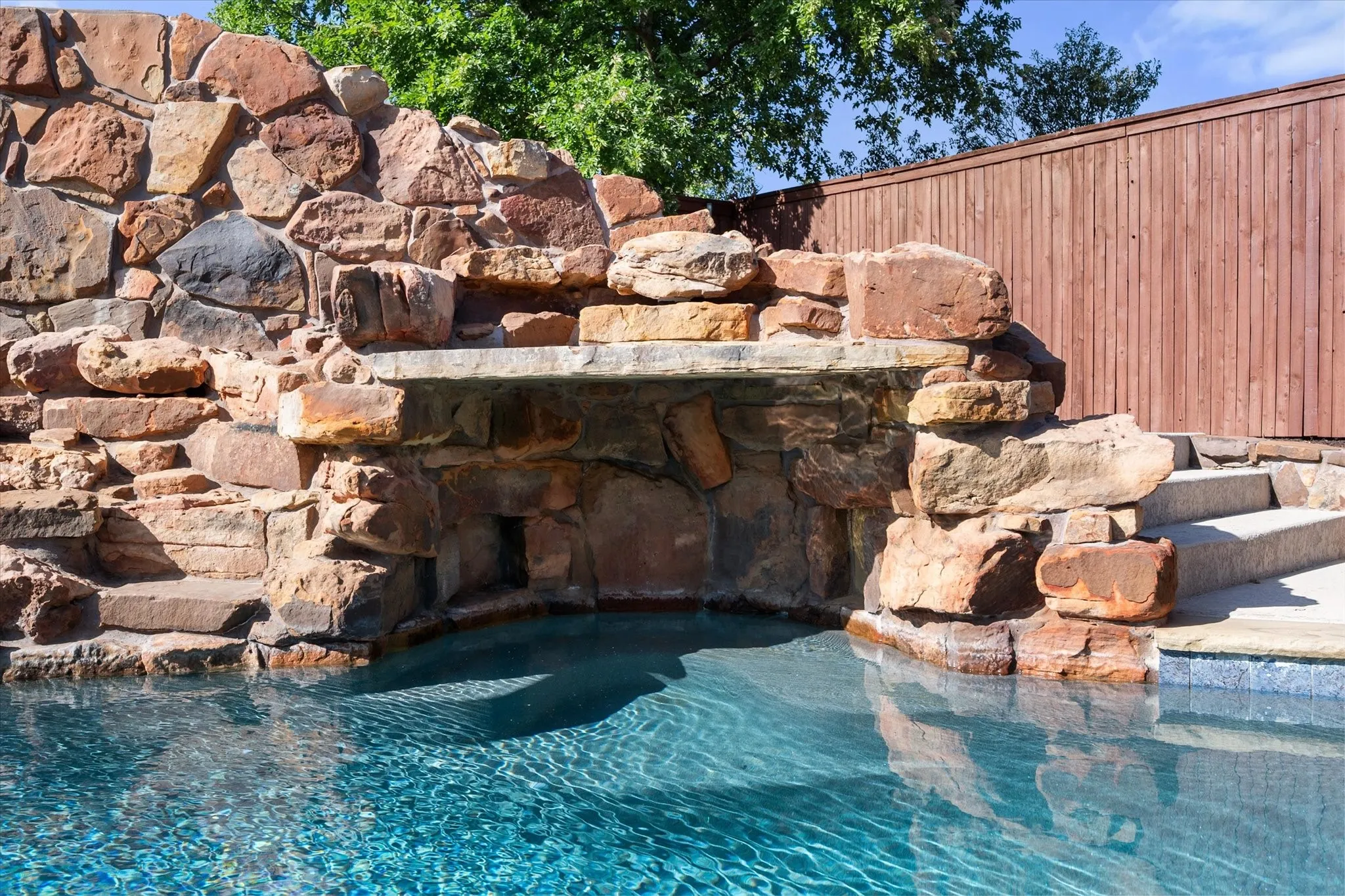 Pool with natural stone grotto, rock waterfall, and integrated stone steps