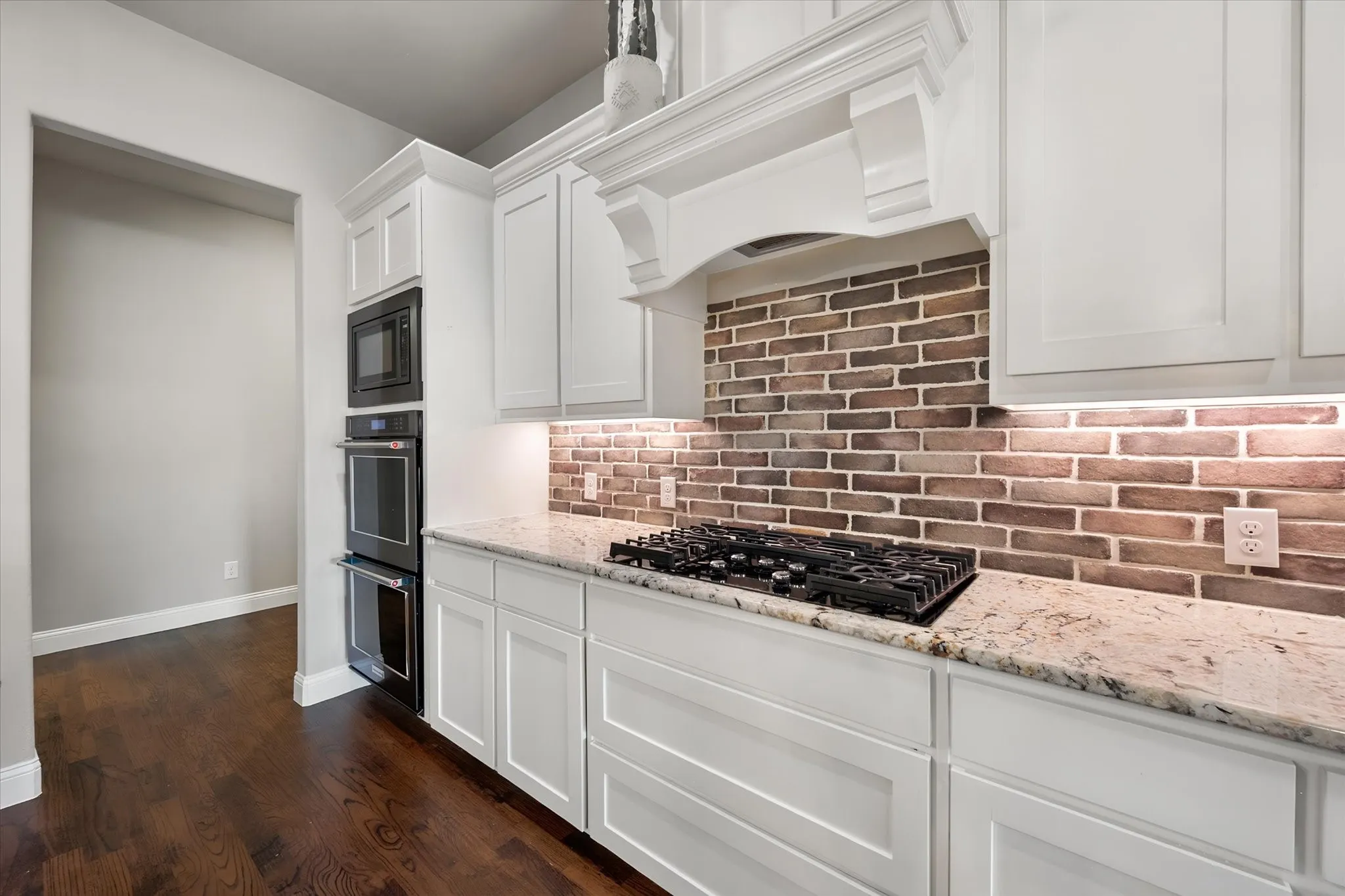 White cabinetry with under-cabinet lighting, granite countertops, and a brick-patterned tile backsplash