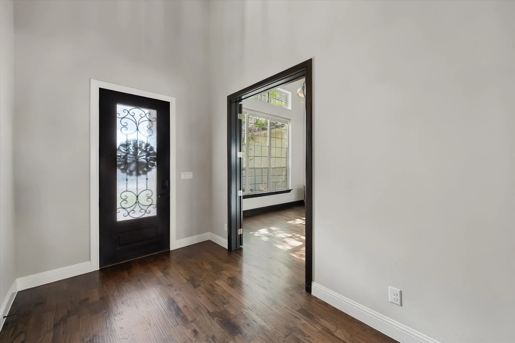 Elegant entryway showcasing rich wood-finish flooring, a decorative black entry door with ornamental glass paneling, and a black-framed interior doorway with glass panels that extends sightlines into adjoining spaces