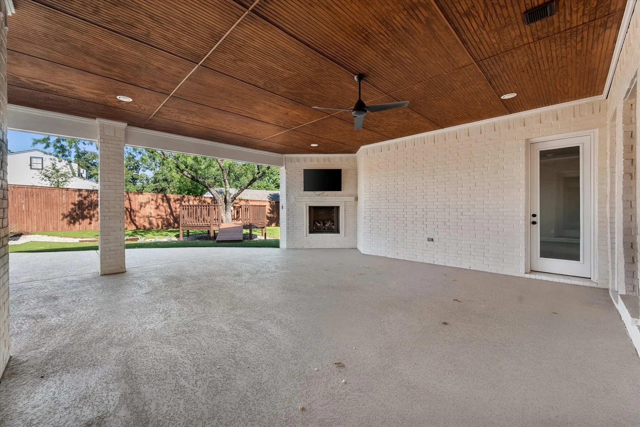 Expansive covered patio featuring a wood-finish ceiling with recessed lighting and ceiling fan, concrete flooring, and white brick construction