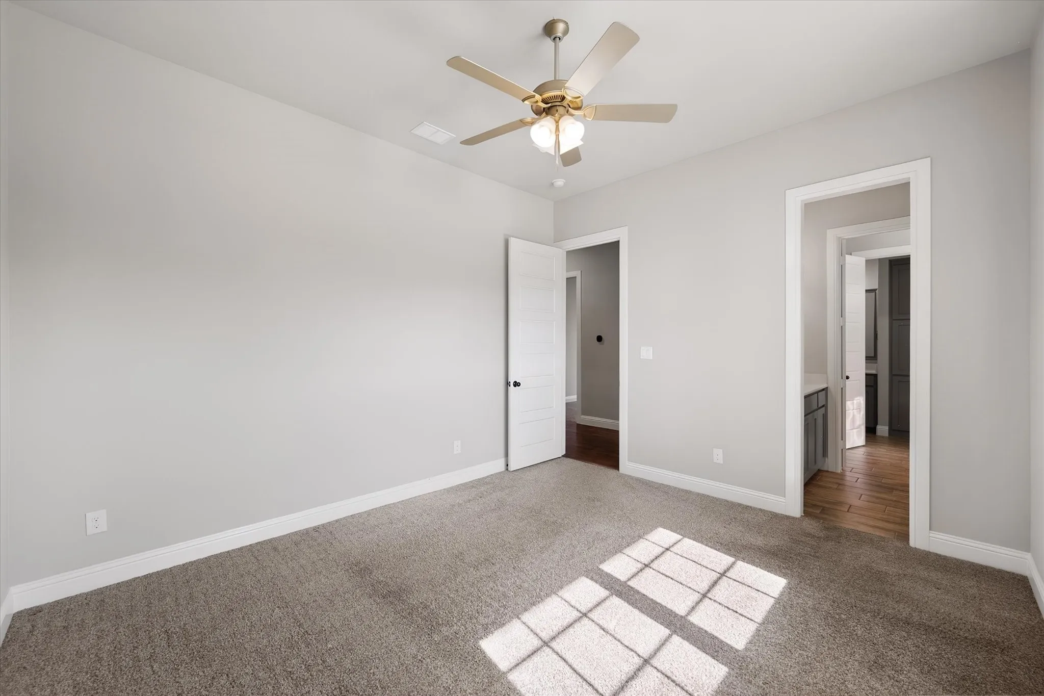 Bright, light-filled bedroom with neutral wall finishes, wood-finish flooring, and ceiling fan with integrated lighting