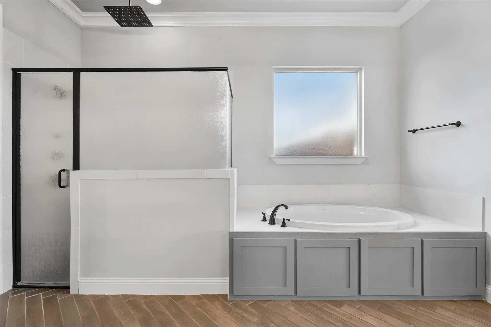 Spa-inspired primary bathroom featuring a gray vanity with multiple storage compartments, a soaking tub with integrated deck, and a frameless glass-enclosed shower with matte black hardware