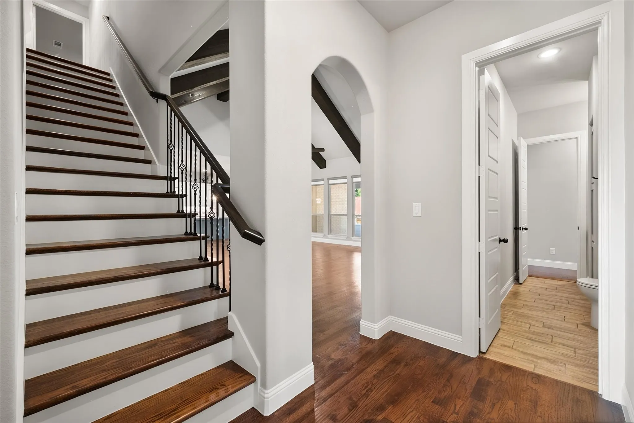 Elegant foyer featuring a curved archway, wood-finish staircase with metal railings, hardwood flooring, and direct access to additional living spaces through white panel doors