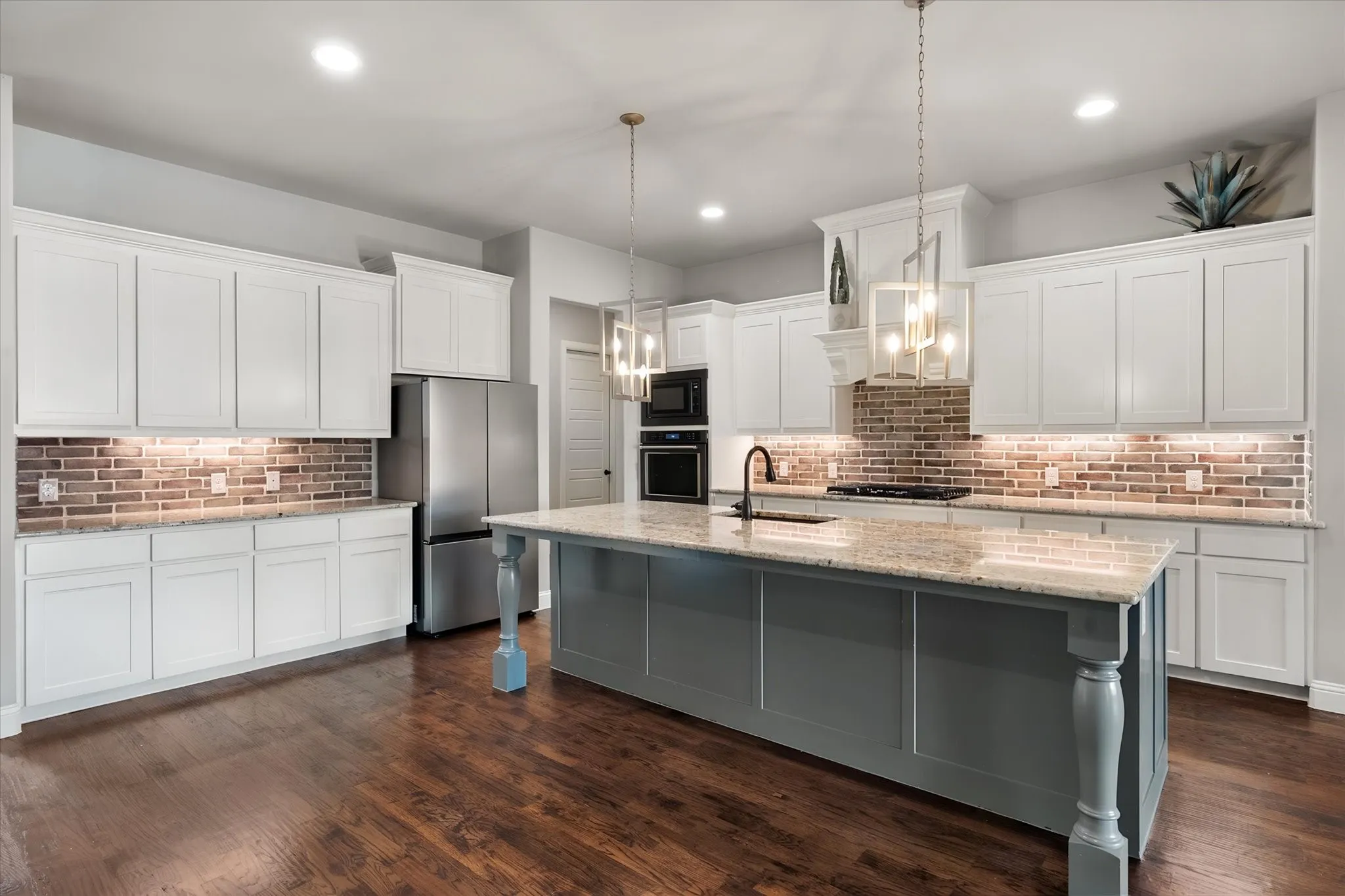 Chef's kitchen featuring white shaker cabinetry, a gray-painted center island with waterfall countertop, stainless steel appliances, and brick backsplash detailing