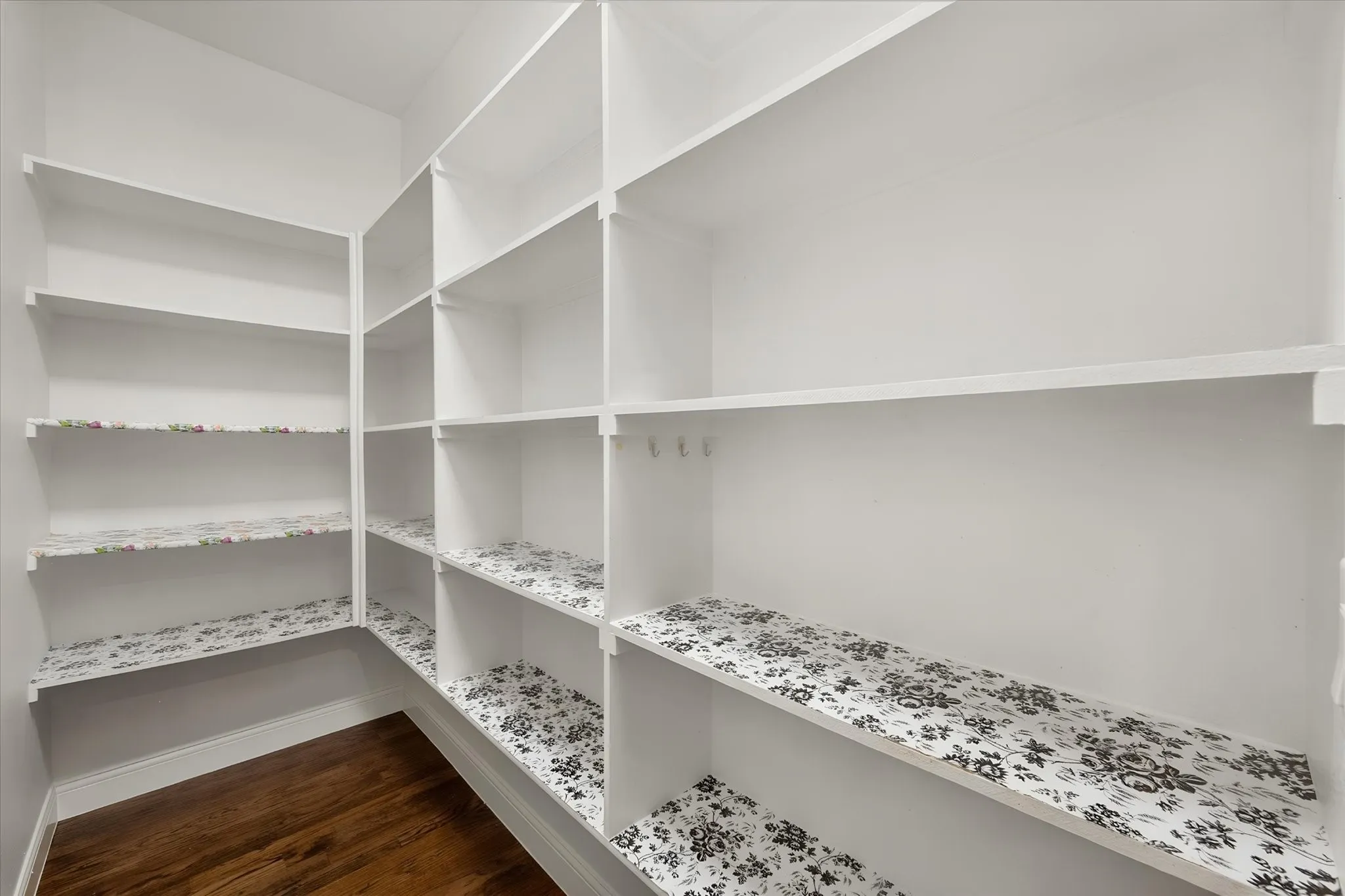 Custom built-in shelving with white painted wood cabinetry and adjustable shelves, featuring patterned fabric-lined backing