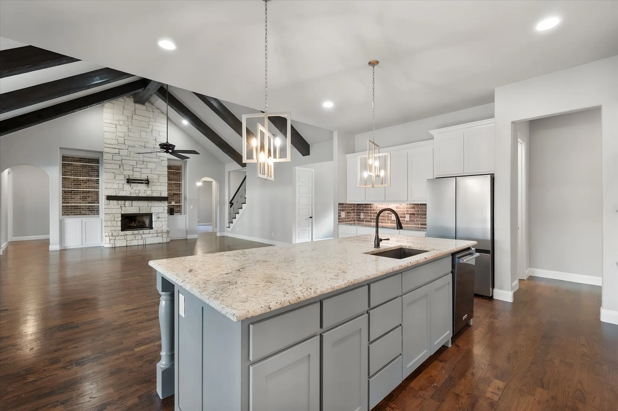 Open-concept kitchen and living area featuring a large center island with light-finish stone countertop, gray cabinetry, and stainless steel appliances