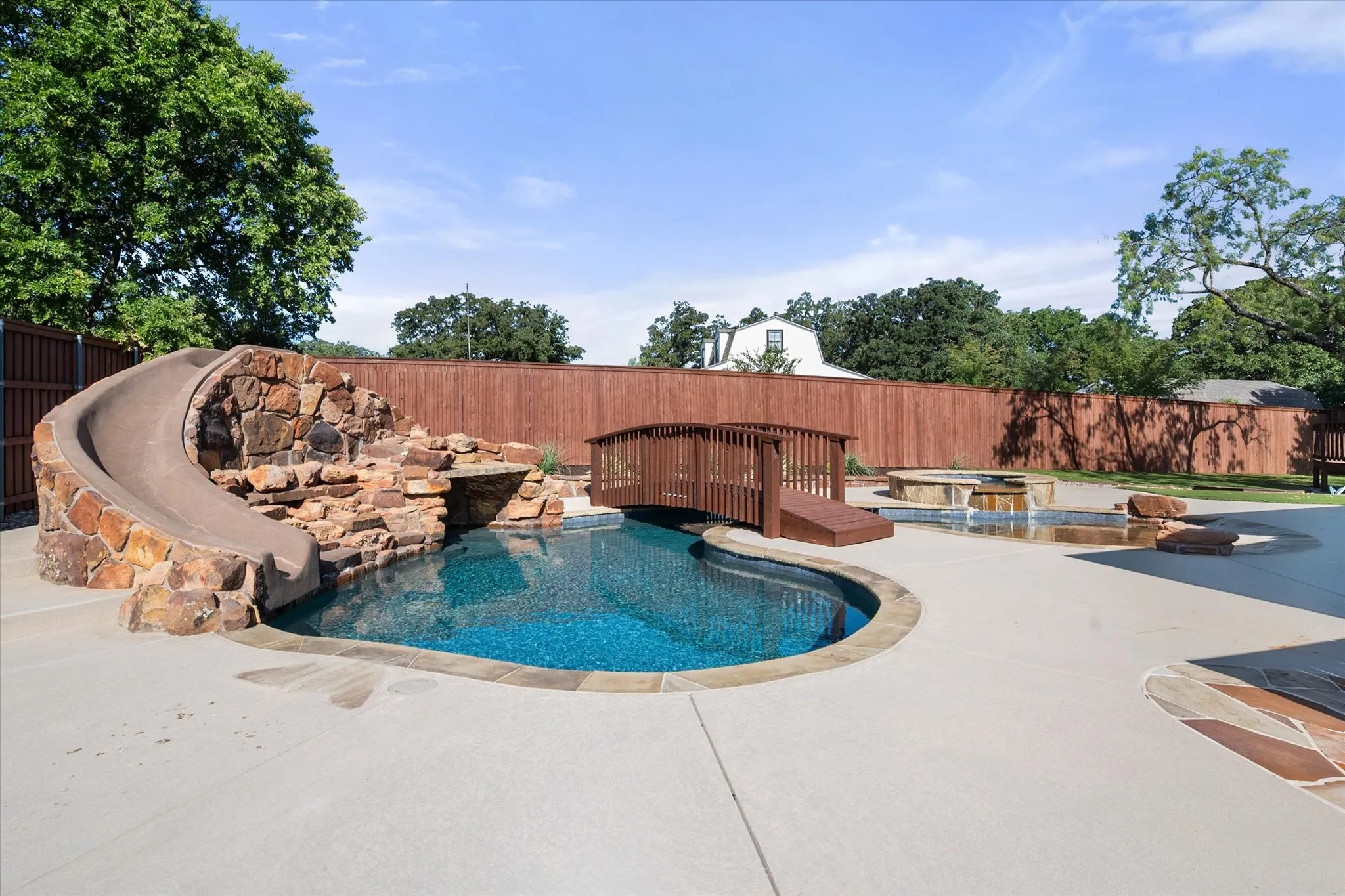 Resort-style saltwater pool featuring a curved design with integrated spa, complemented by a dramatic copper-finish water feature and natural stone accents