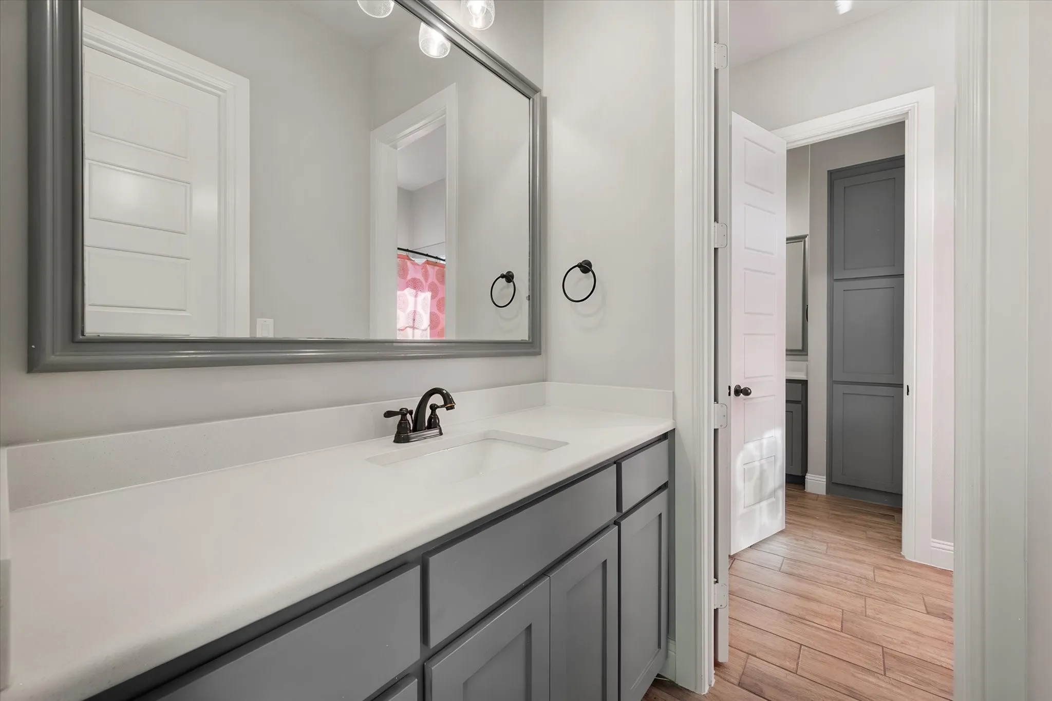 Elegant primary bathroom featuring a gray vanity with ample countertop storage, white quartz countertop surface, matte black faucet fixtures, and a large framed mirror