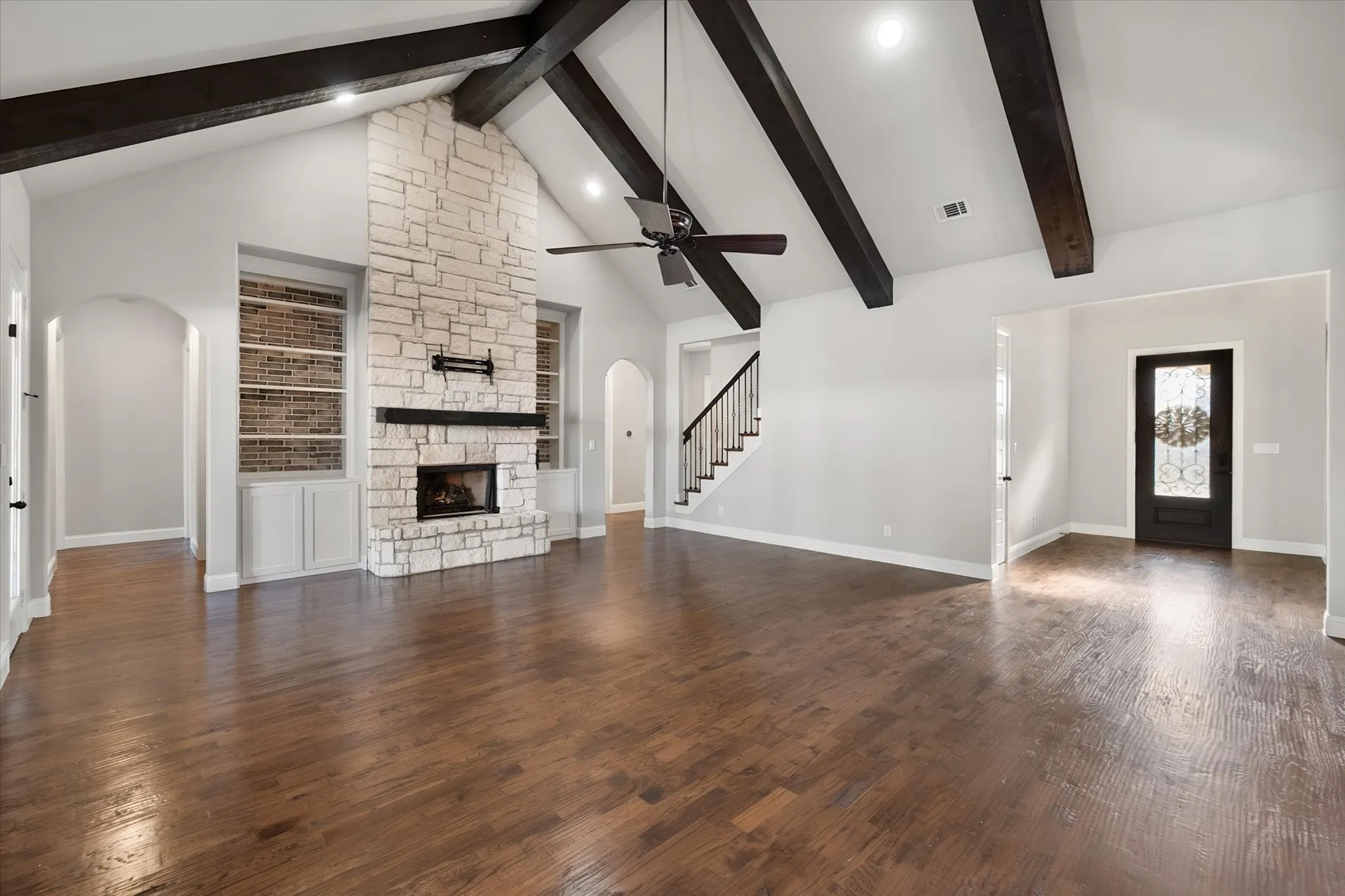 Expansive great room showcasing vaulted ceilings with exposed dark wood beams, abundant natural light, and wide-plank wood-finish flooring throughout