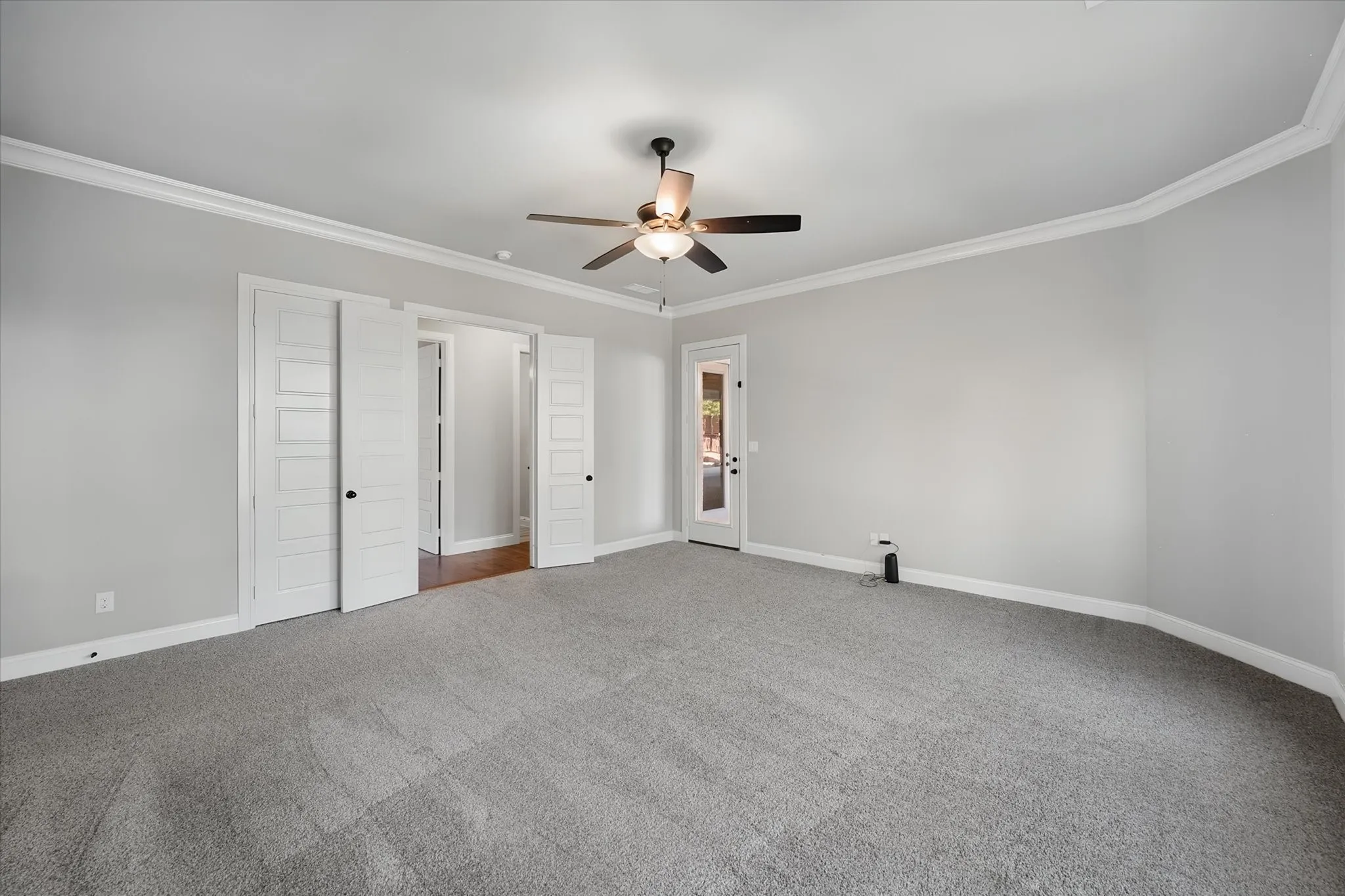 Spacious primary bedroom featuring neutral wall finishes, curved ceiling detail with ceiling fan, and multiple closet entries with louvered doors