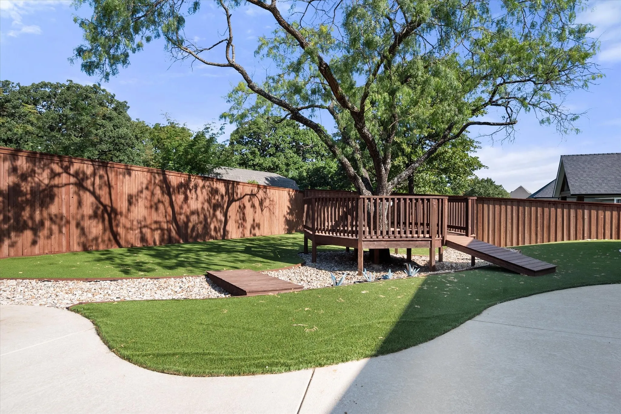 Expansive backyard oasis featuring a mature shade tree, manicured lawn, brick privacy fencing, and a composite deck with railings