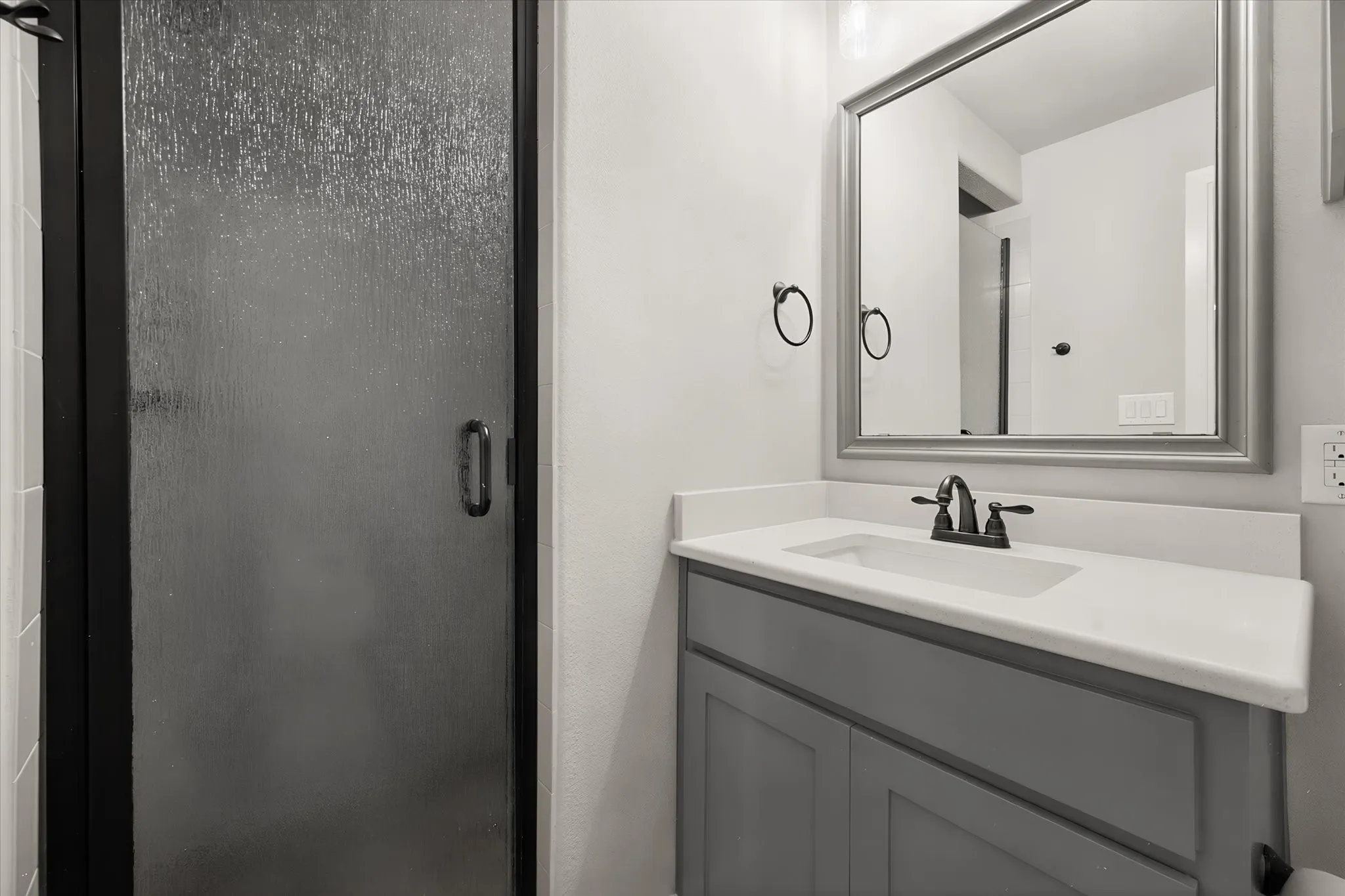 Modern bathroom featuring a gray vanity with white quartz countertop, matte black faucet, and framed mirror