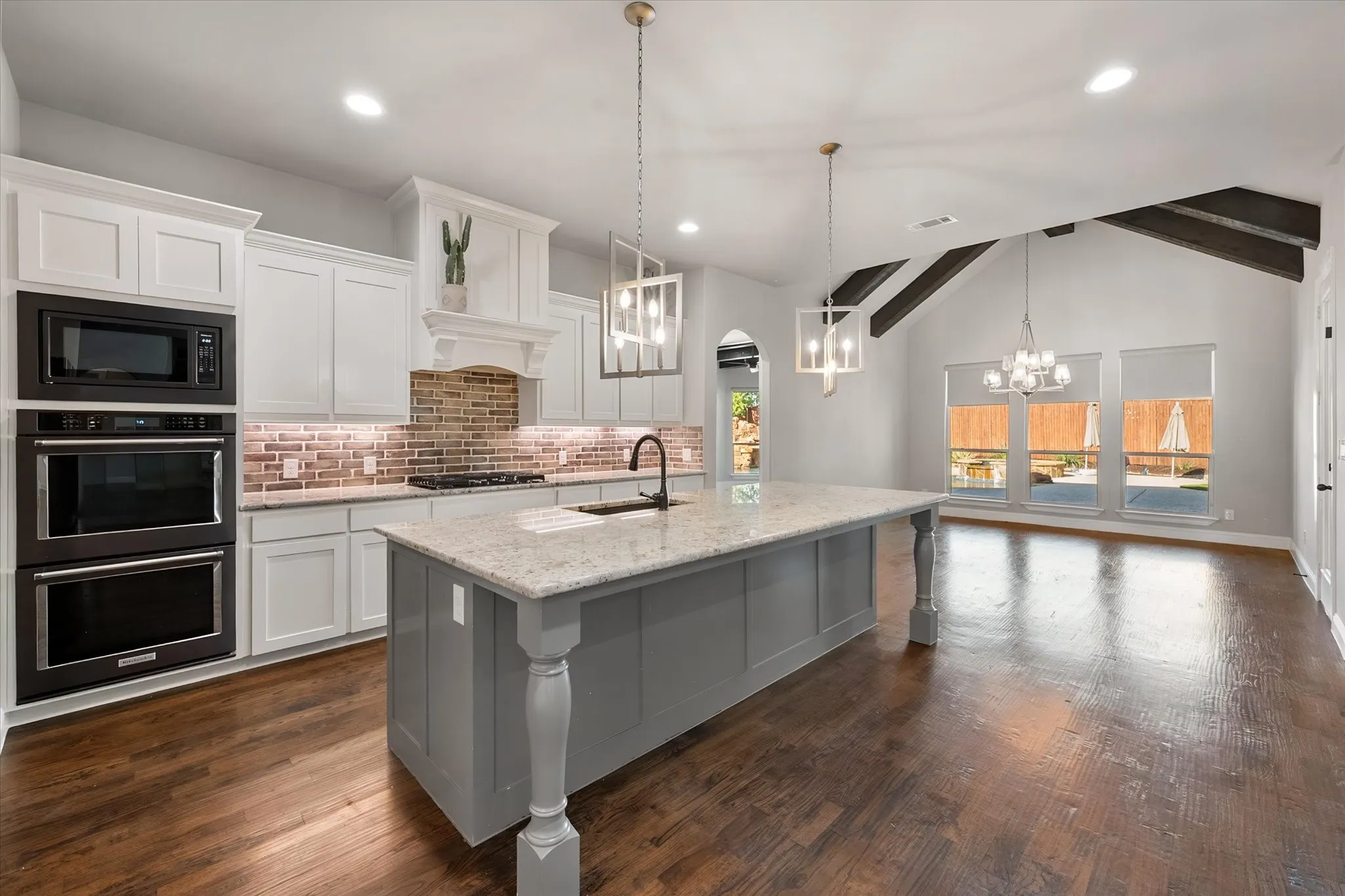 Chef's kitchen featuring white cabinetry, stainless steel double wall ovens, and a gray center island with white marble countertops and pendant lighting