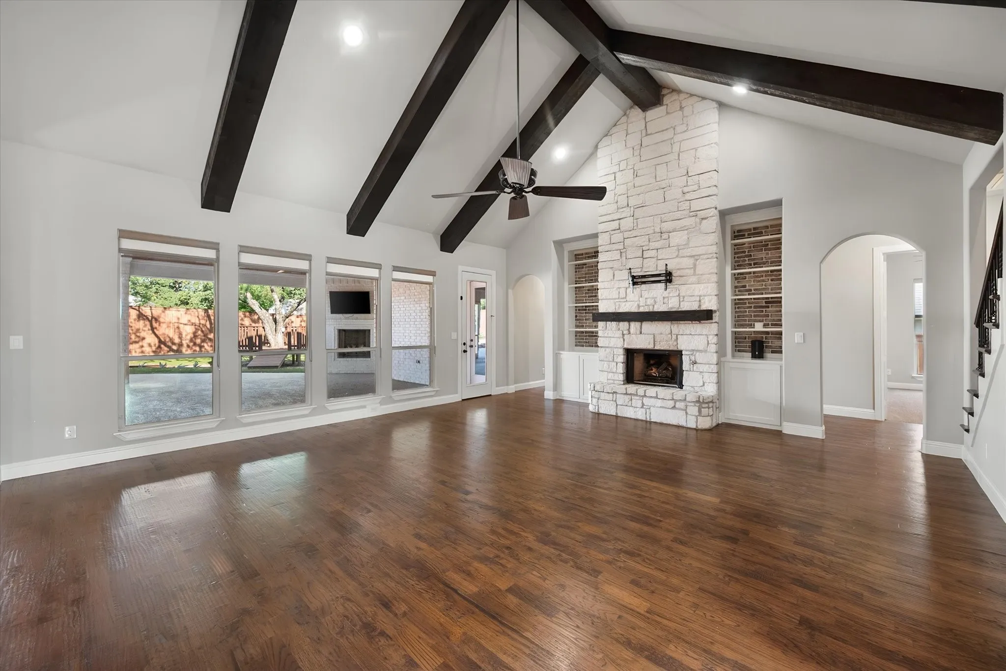 Spacious open-concept living area featuring exposed ceiling beams, a ceiling fan, and abundant natural light from French doors and transom windows