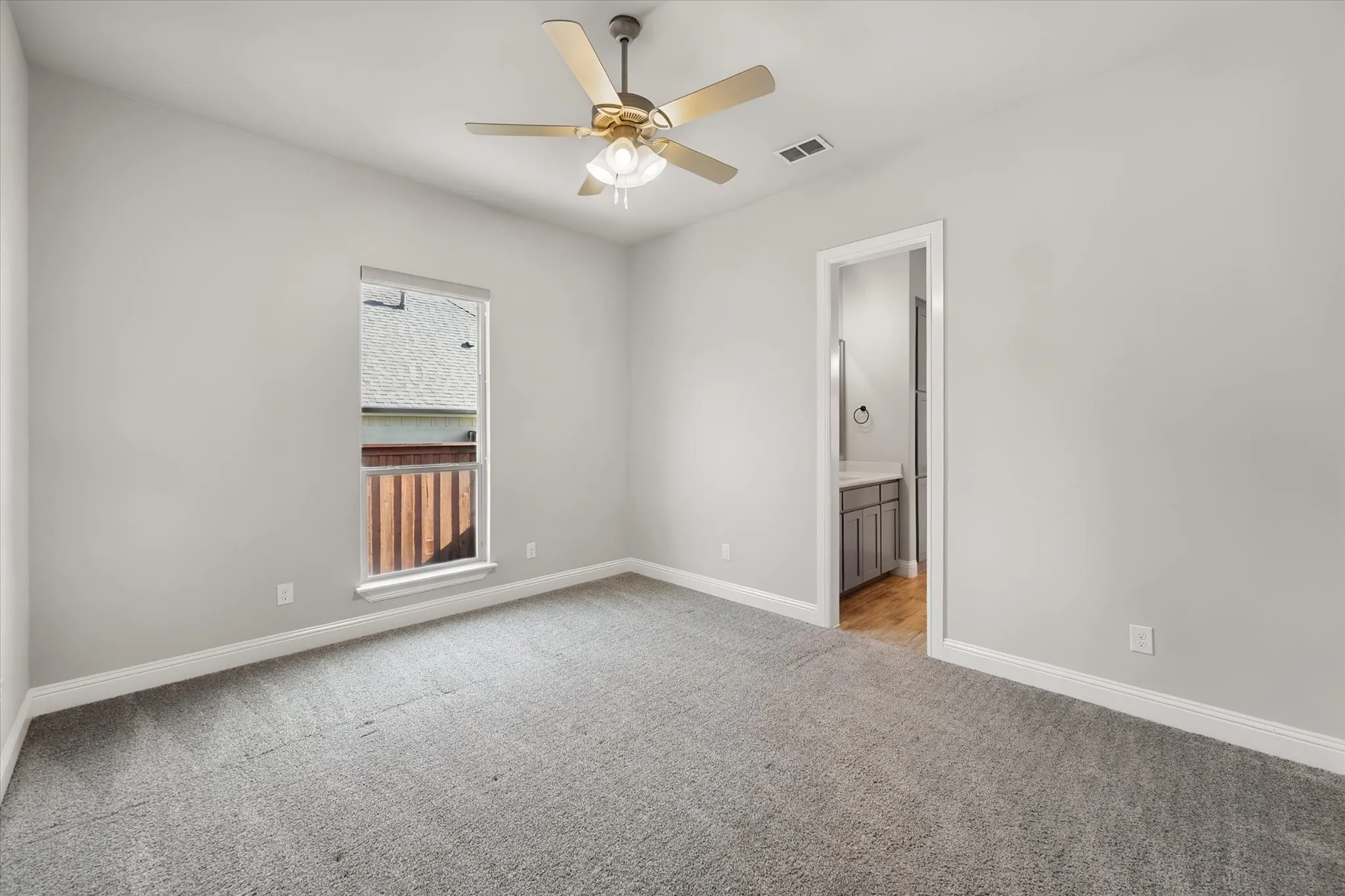Spacious bedroom with neutral wall finishes, plush carpeting, and a ceiling fan with integrated lighting