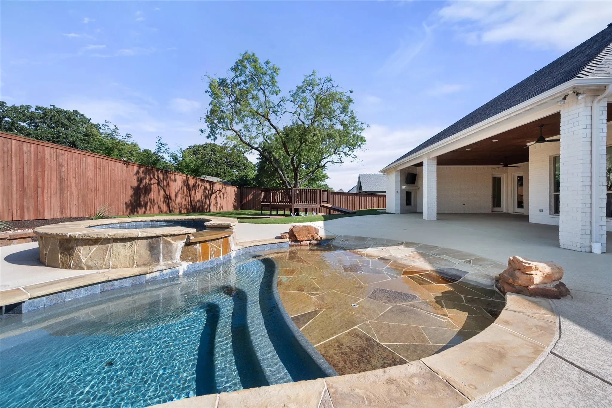 Expansive backyard oasis featuring a resort-style swimming pool with curved water feature, integrated spa, and stone decking