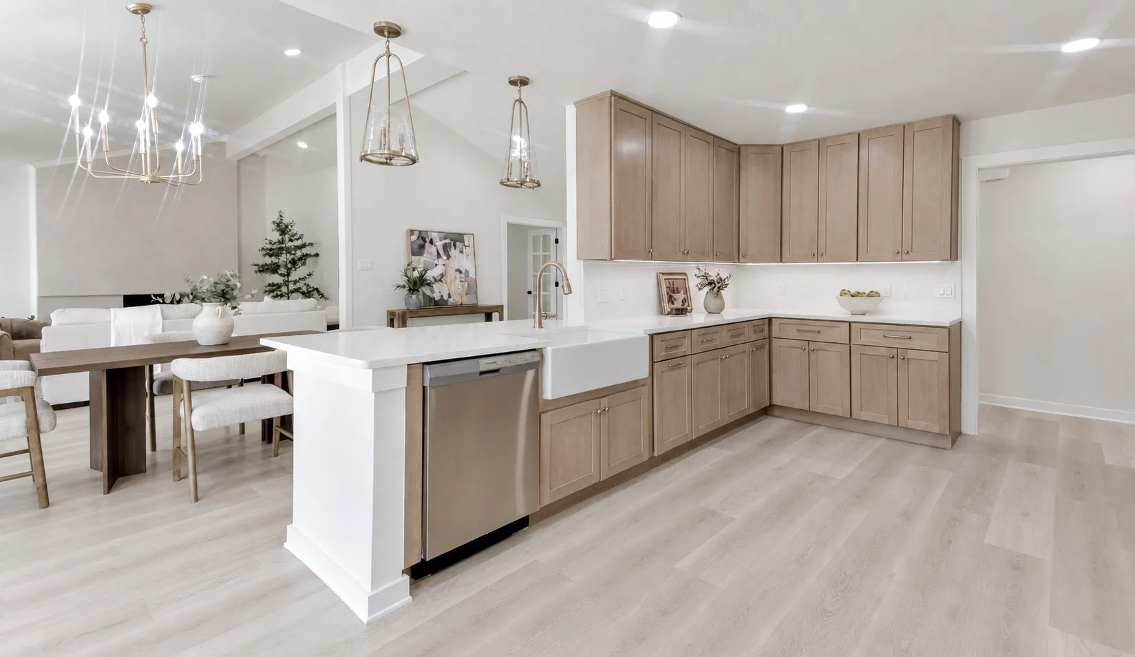 Wide Open-concept kitchen featuring light wood-finish flooring, white quartz countertops, a large farmhouse sink, and stainless steel appliances
