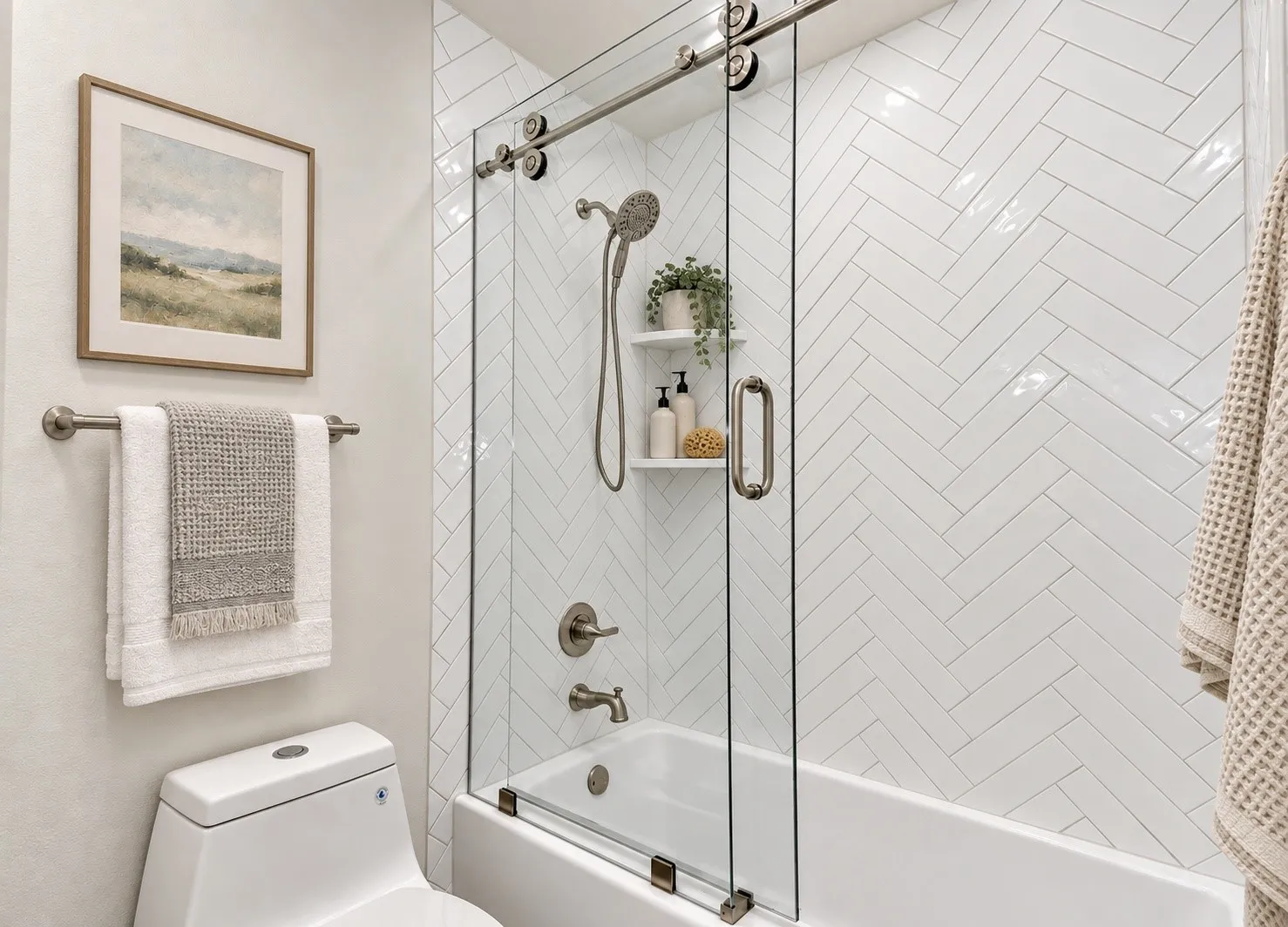 Herringbone tile shower surround, integrated bathtub, sliding glass shower door and a recessed shower shelf