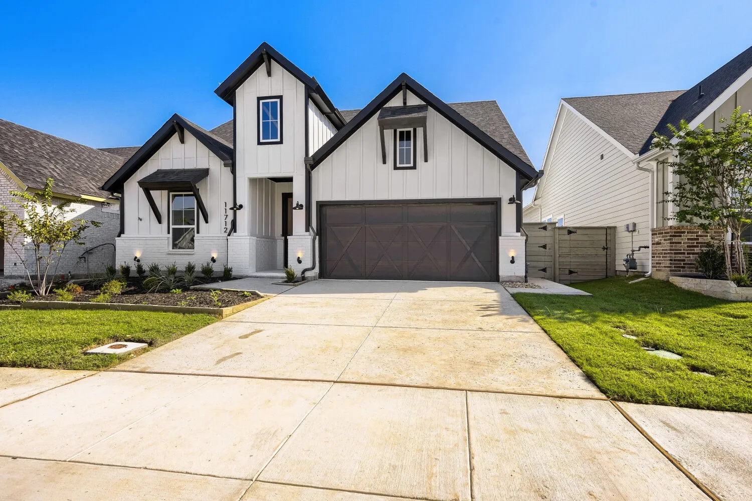 Modern farmhouse exterior featuring board and batten siding, dark trim accents, a two-car garage with a carriage-style door, an extended concrete driveway, and established landscaping