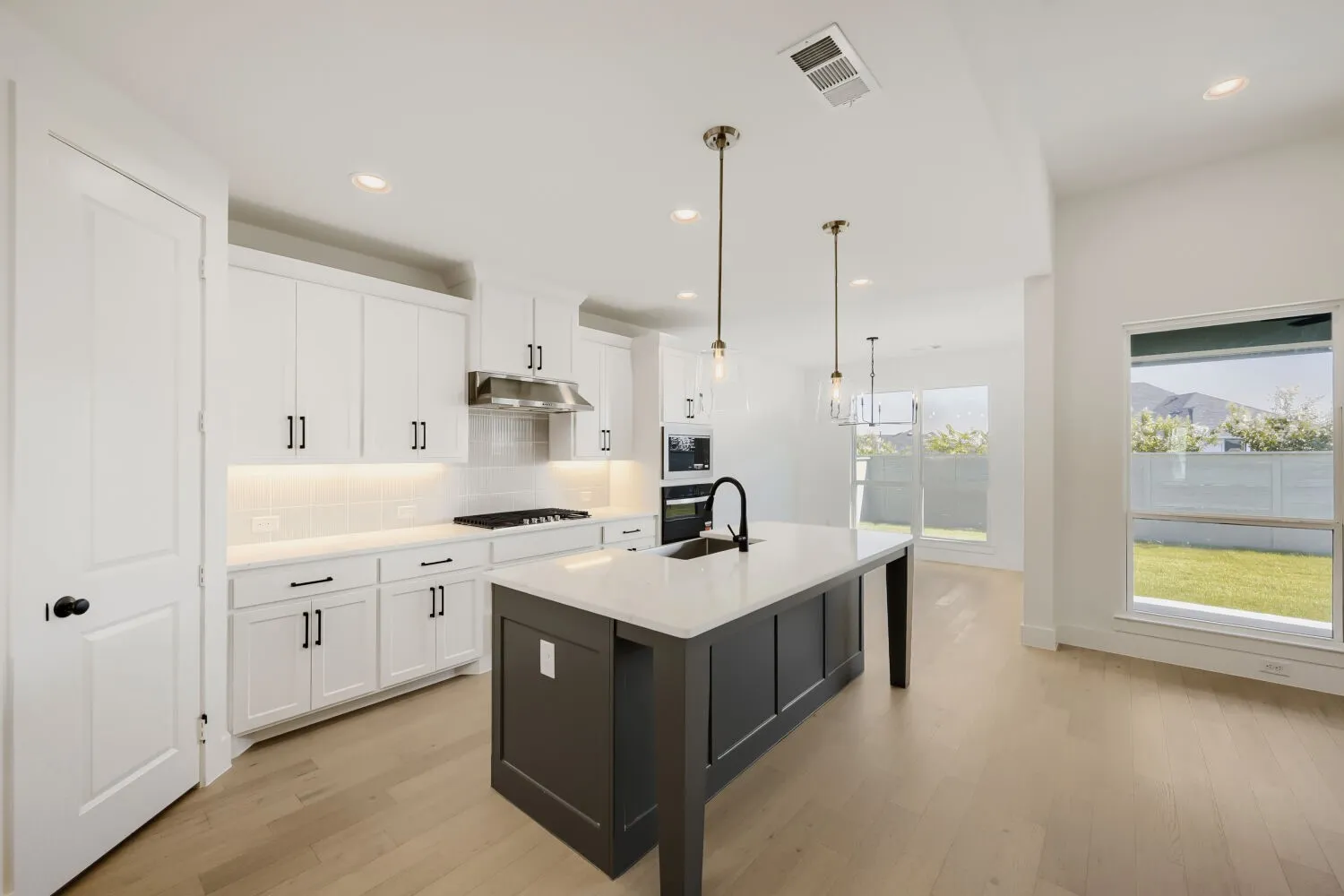 Contemporary kitchen with white cabinetry, a dark-toned island, and light wood-finish flooring