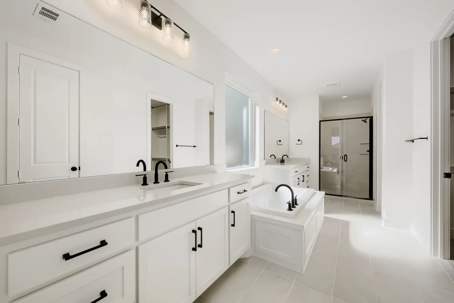 Dual vanity with undermount sinks, built-in soaking tub with matte black fixtures, separate glass-enclosed shower, and tiled flooring