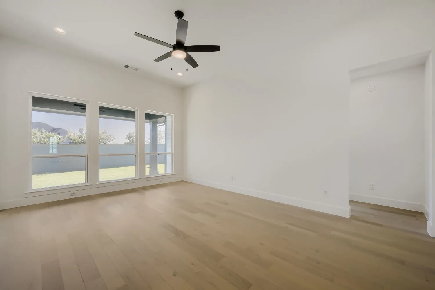 Vaulted ceiling with recessed lighting, wood-finish flooring, three large windows, and a ceiling fan