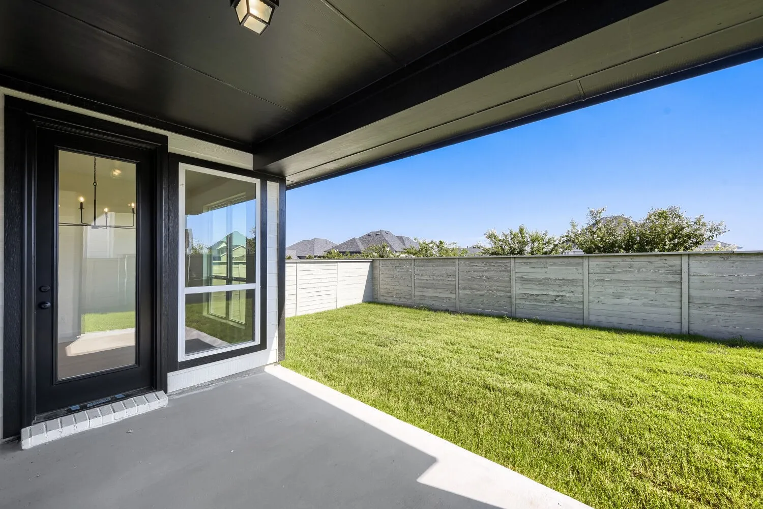 Covered outdoor patio with a concrete surface, leading to a landscaped lawn