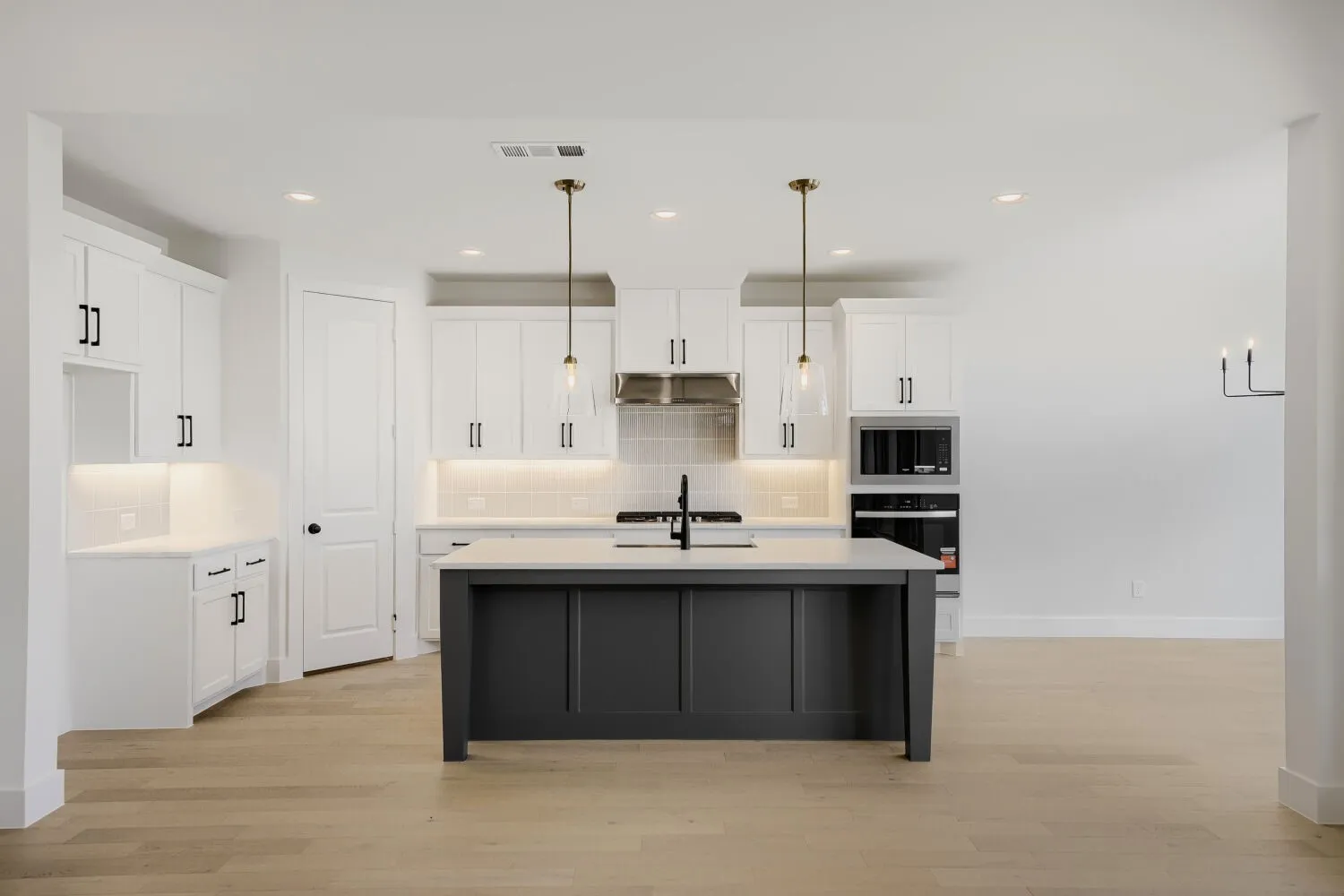 Kitchen featuring white shaker-style cabinetry, a dark-toned island, stainless steel appliances, and wood-finish flooring