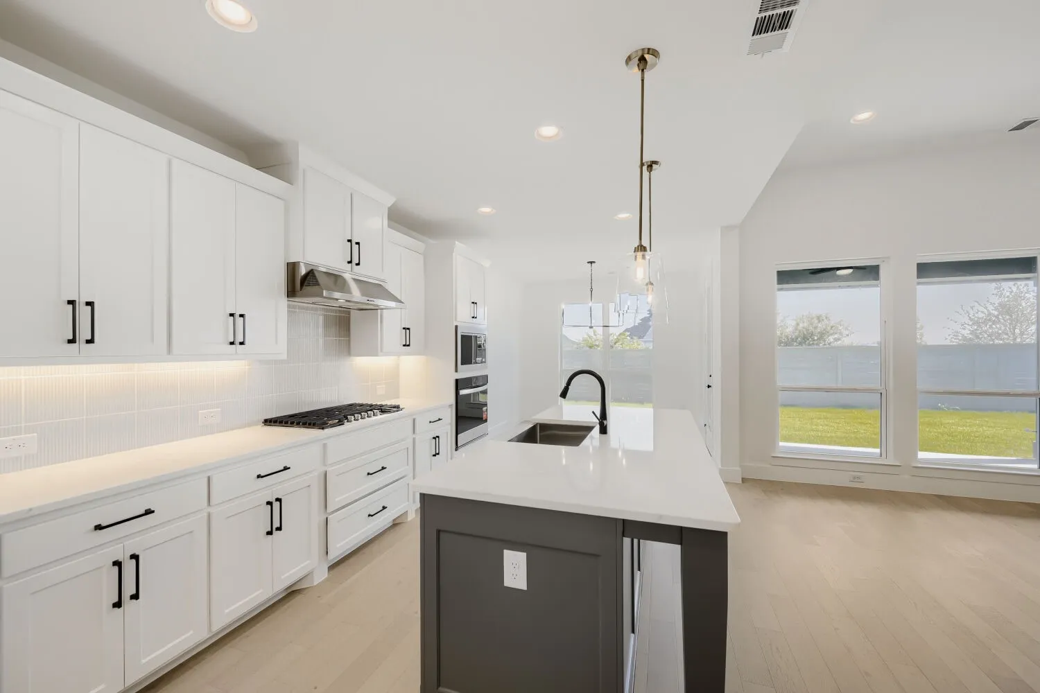 White shaker-style cabinetry with black hardware, gas cooktop with stainless steel range hood, built-in double ovens, center island with undermount sink, and wood-finish flooring