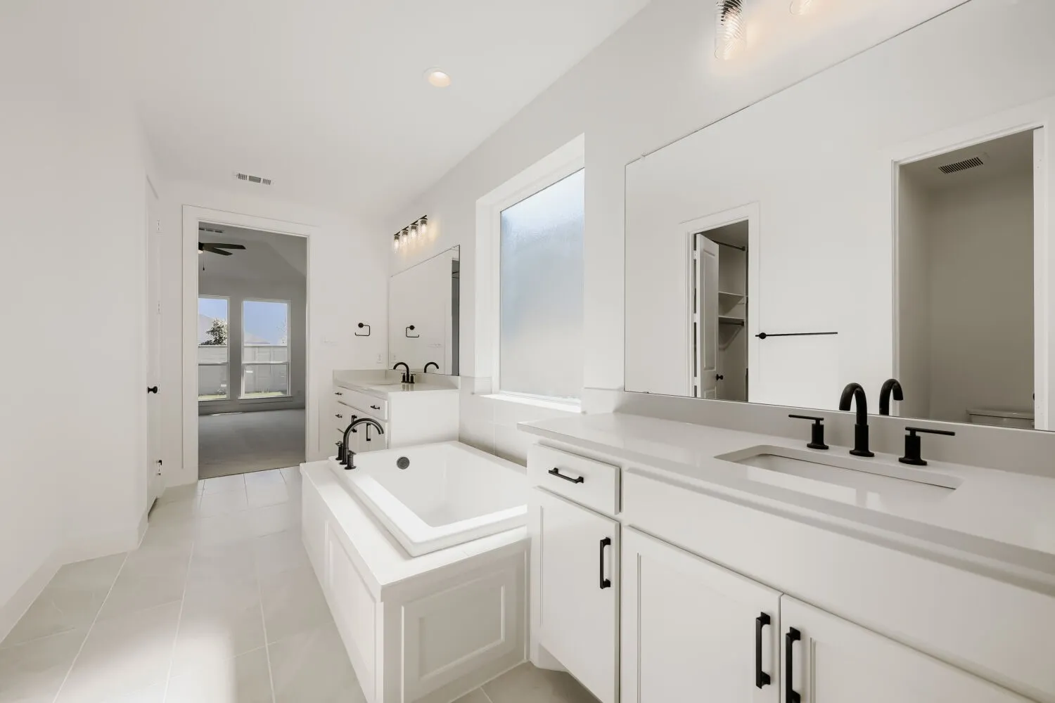 Built-in soaking tub, dual vanity with undermount sinks, stone countertops, matte black plumbing fixtures, and white cabinetry