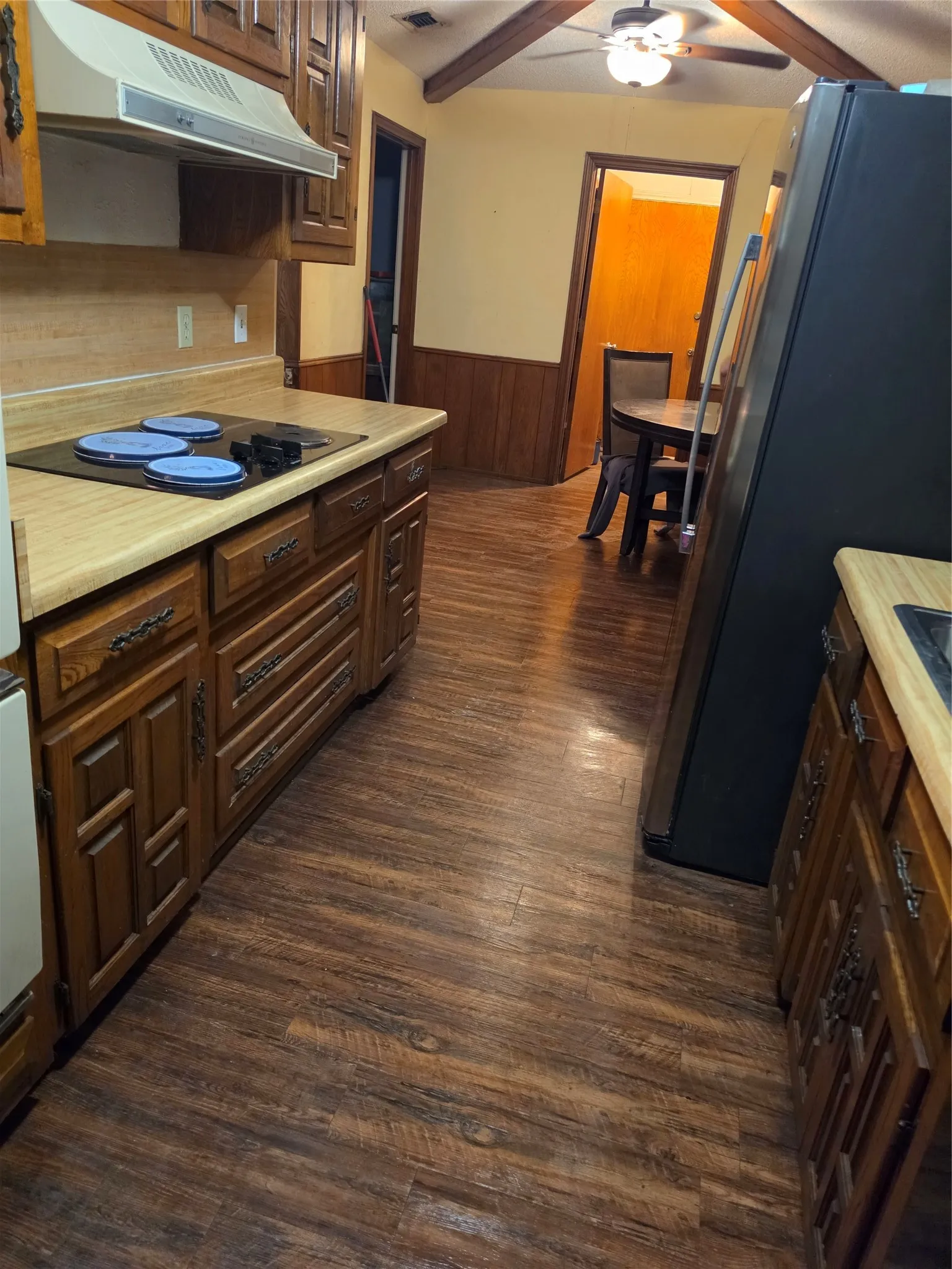 Wood-finish flooring throughout, wood paneling, wood beam ceiling details, built-in wooden cabinetry, and a ceiling fan with integrated lighting