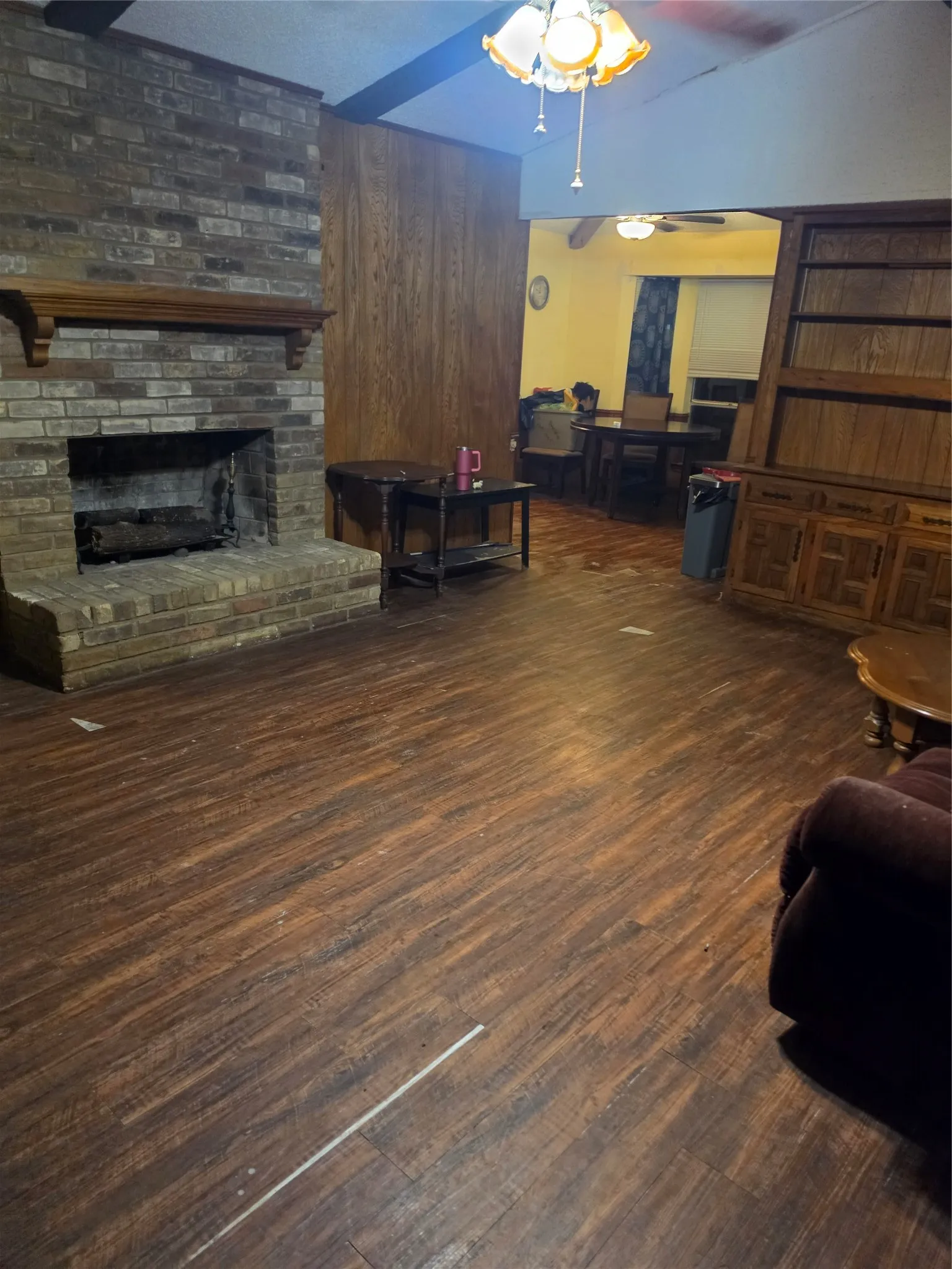 Brick fireplace with wood mantel, wood-finish flooring, wood paneling, and a ceiling-mounted light fixture