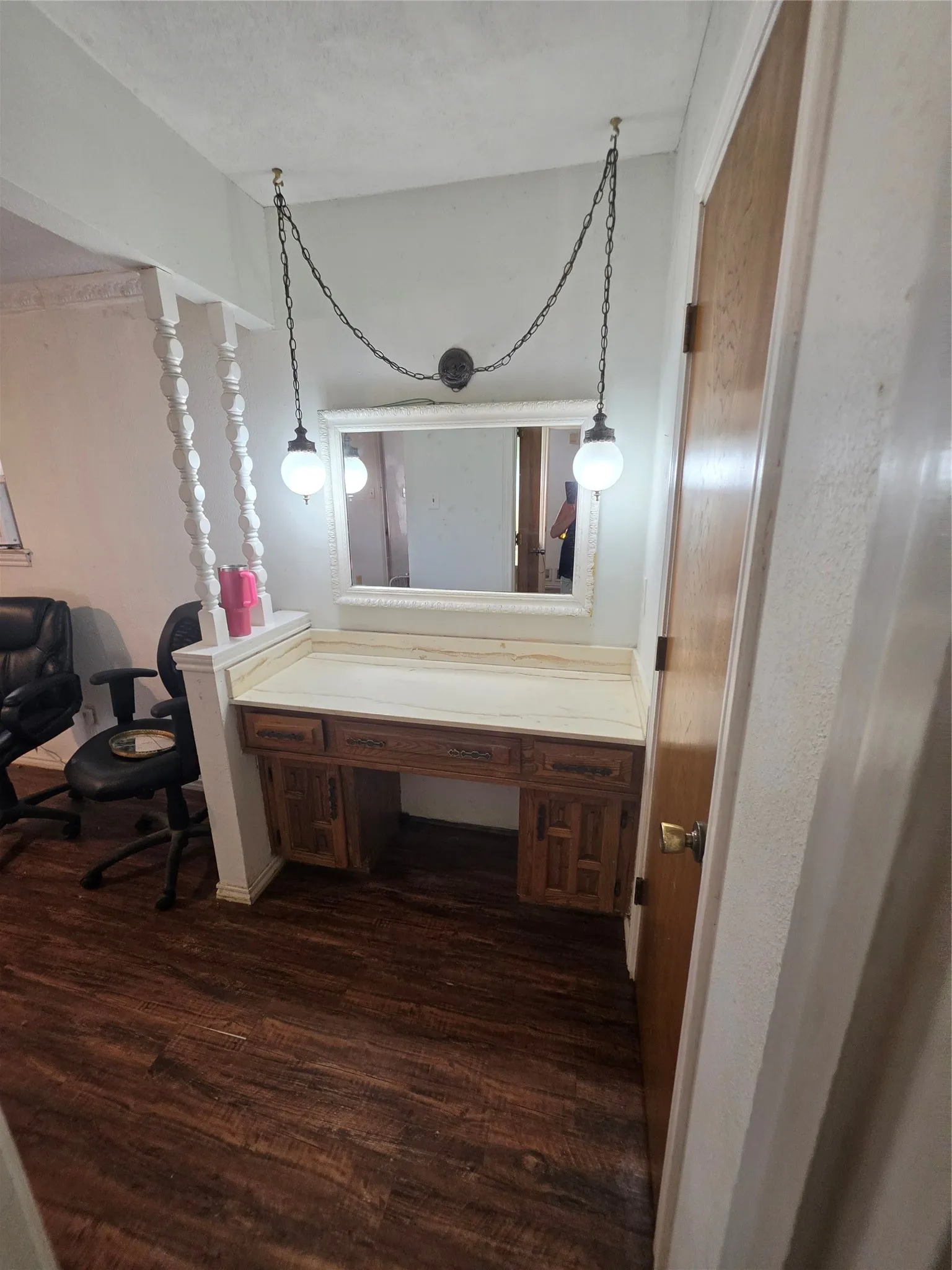 Built-in wood-finish desk with a light-toned countertop, framed mirror, and suspended spherical light fixtures