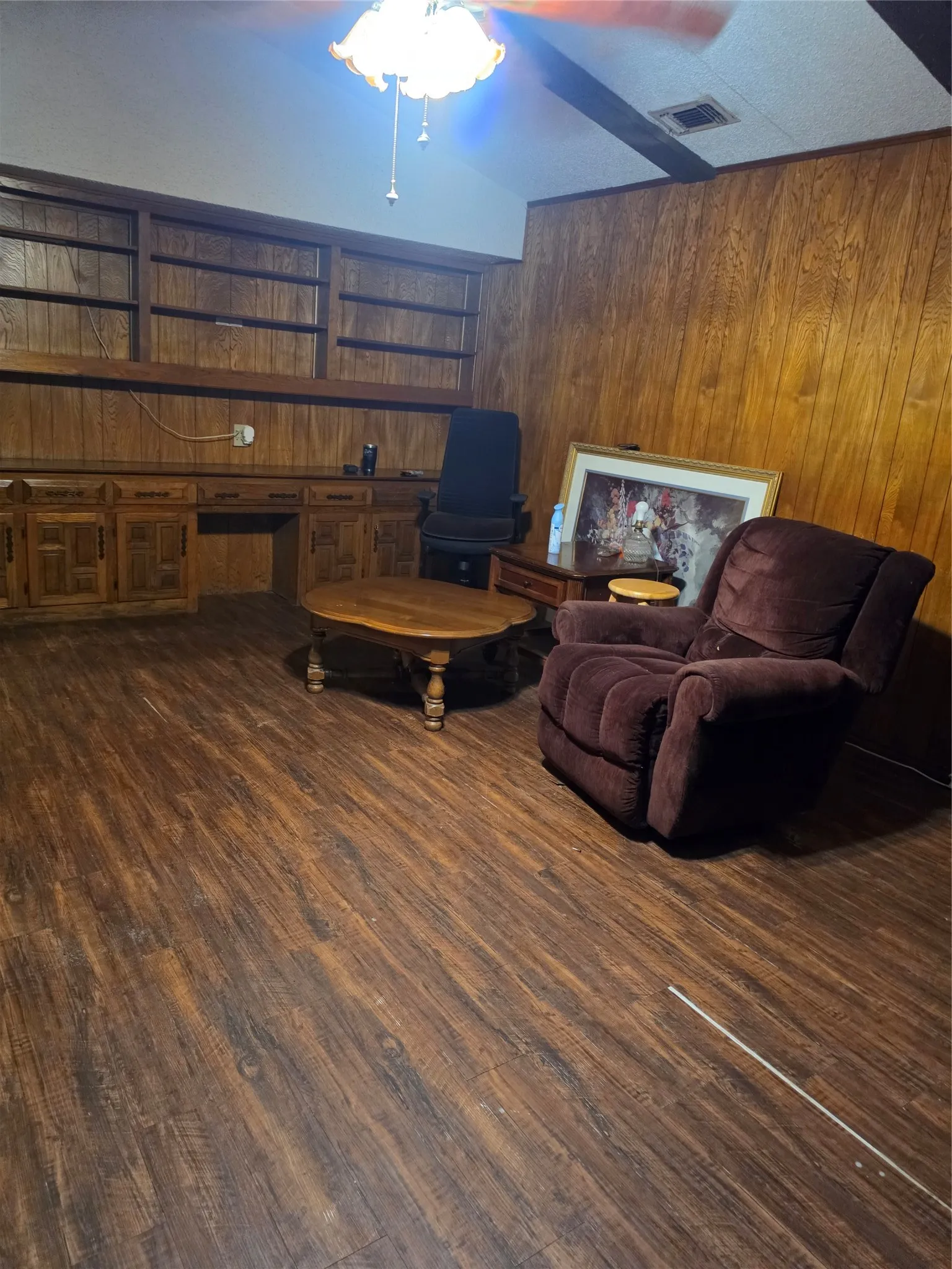 Spacious recreation room featuring rich wood-finish flooring, wood-paneled walls, and built-in cabinetry with multiple shelving units
