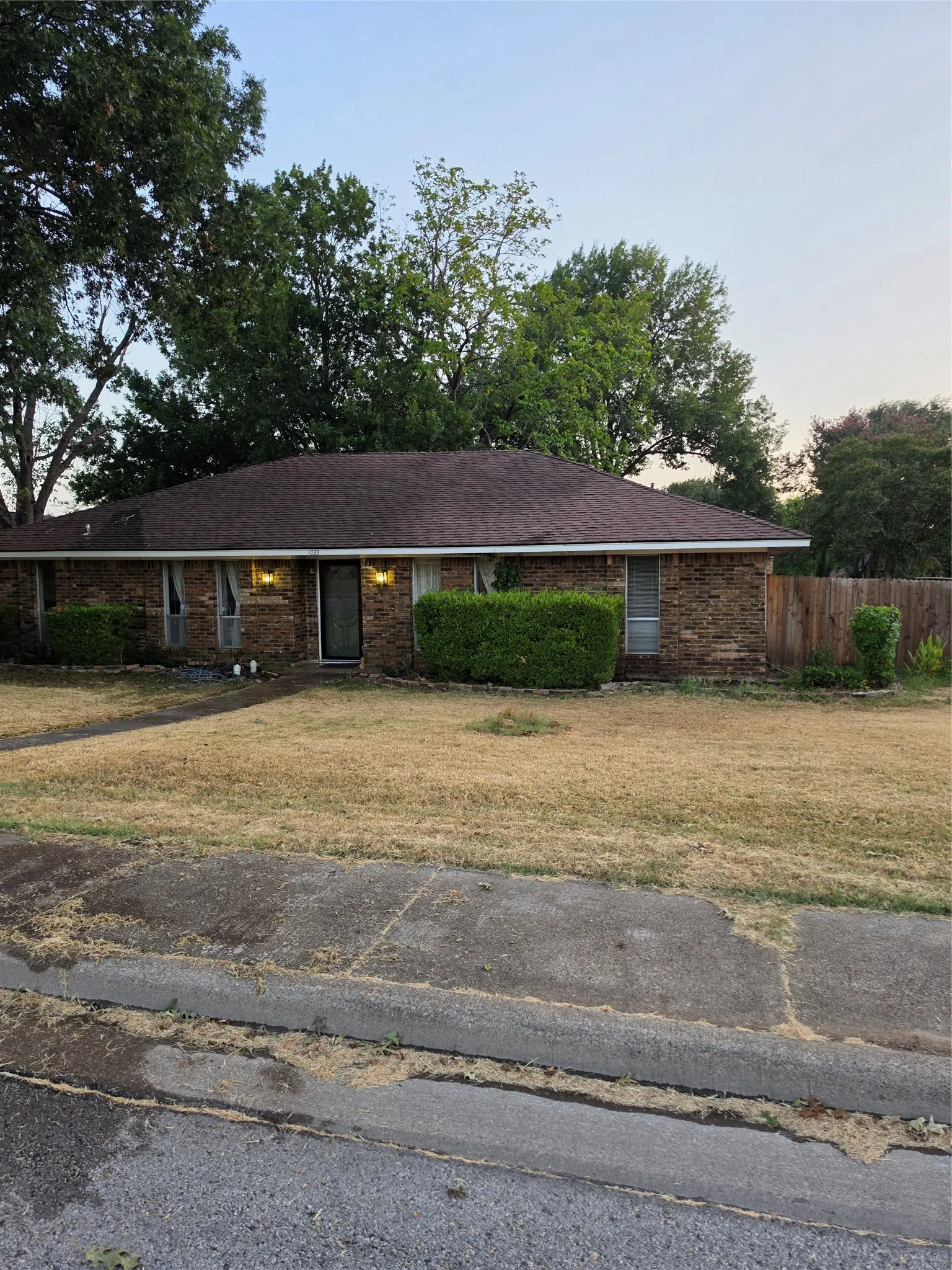 Brick ranch-style home featuring a covered front porch, multiple windows with natural light, and a spacious front-facing lawn with mature landscaping and established trees