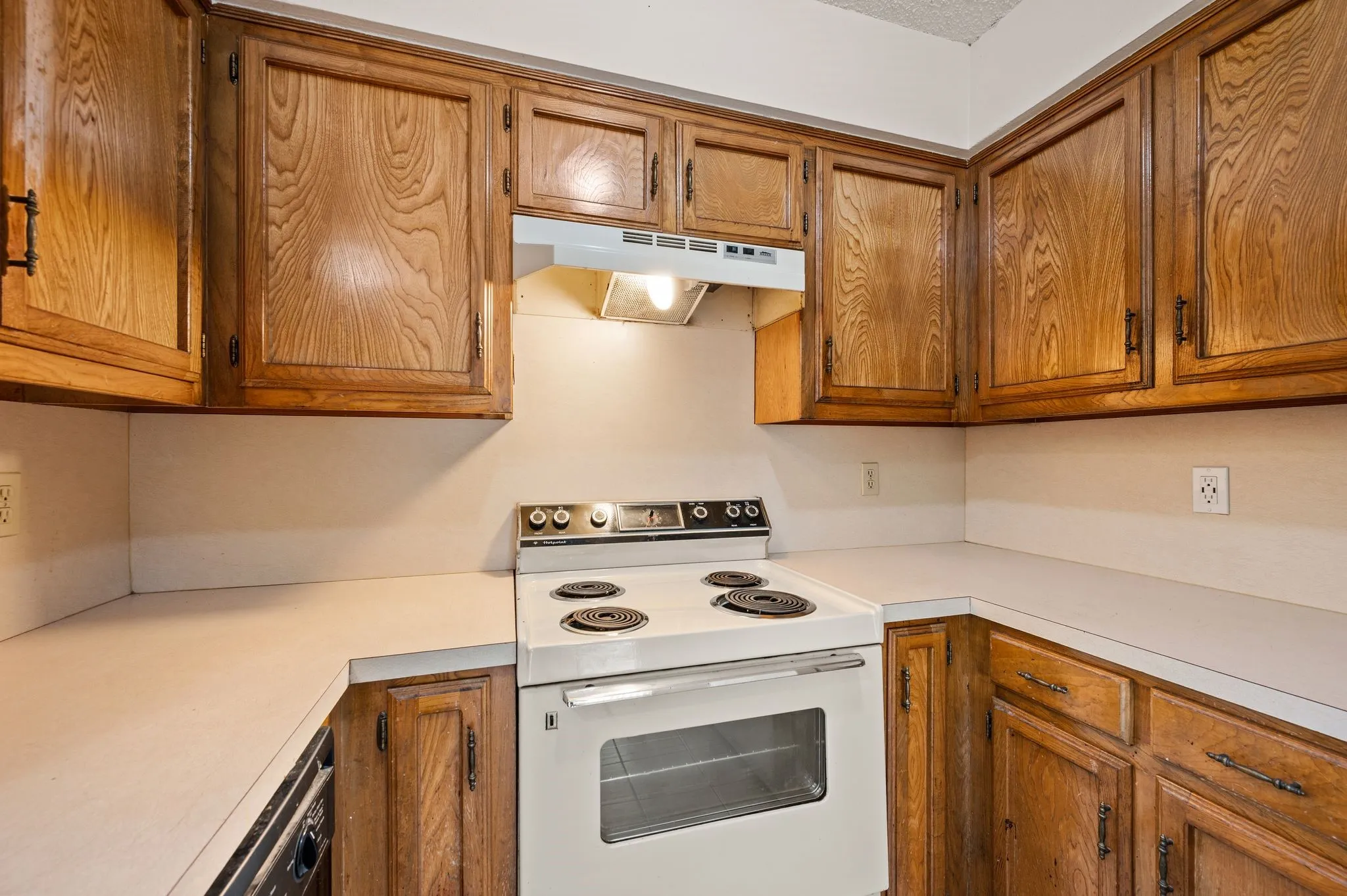Wood-finish cabinetry with dark hardware, white countertops, and a white electric range with an overhead vent