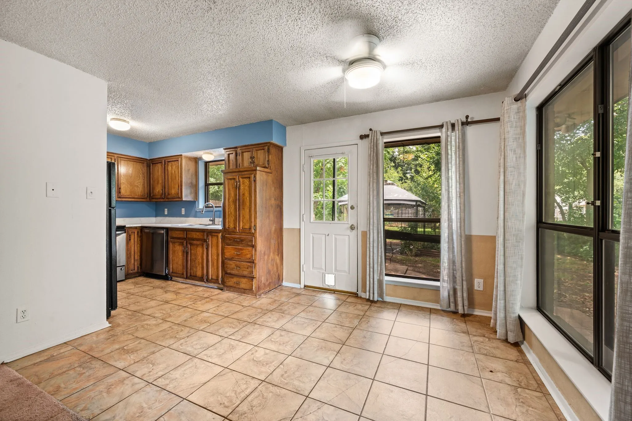 Kitchen and dining area featuring tile flooring, wood cabinetry, a stainless steel dishwasher, and a ceiling fan