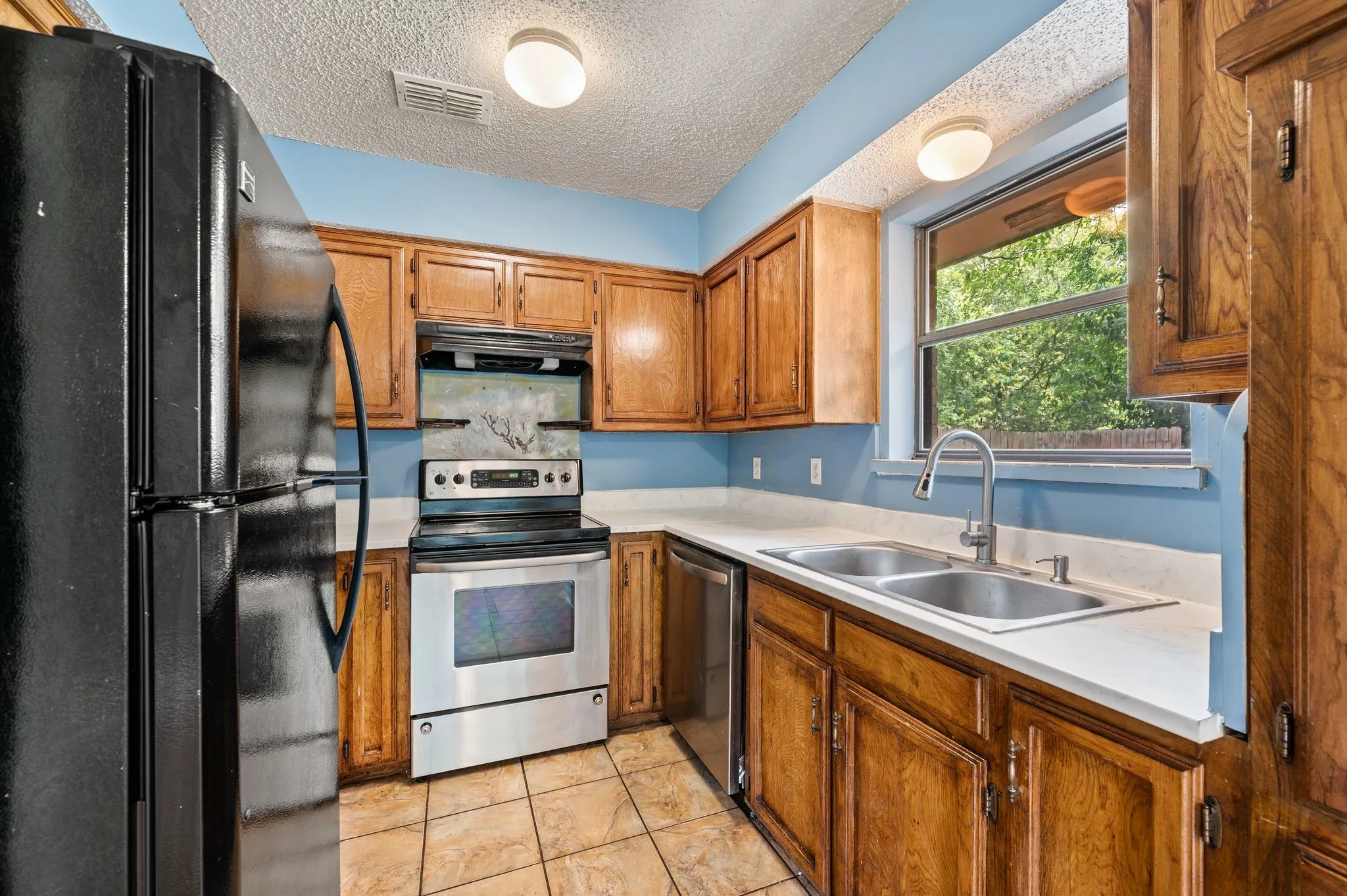 Wood-finish cabinetry paired with light countertops, a stainless steel electric range, and a dual basin sink