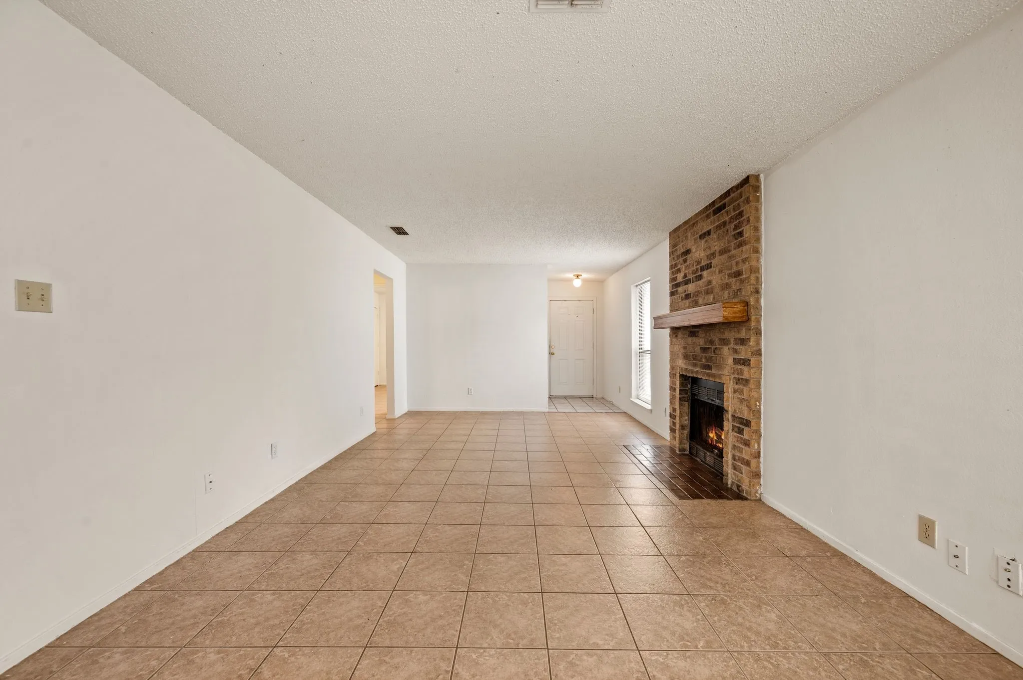 Tiled flooring throughout, brick fireplace with a wood mantel, and white walls