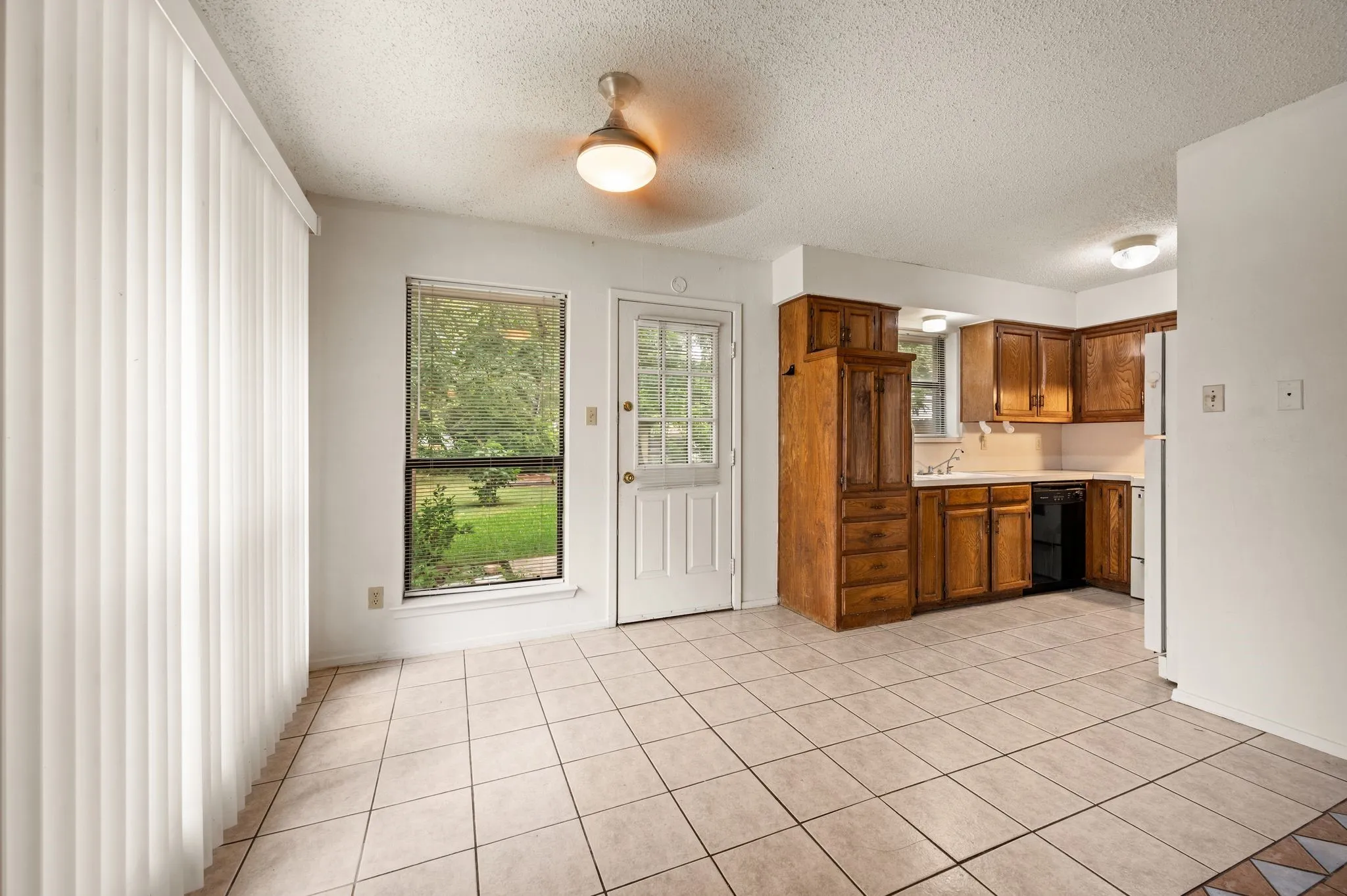 Neutral tone ceramic tile flooring, wood cabinetry with integrated storage, white appliances, and a ceiling fan with integrated lighting