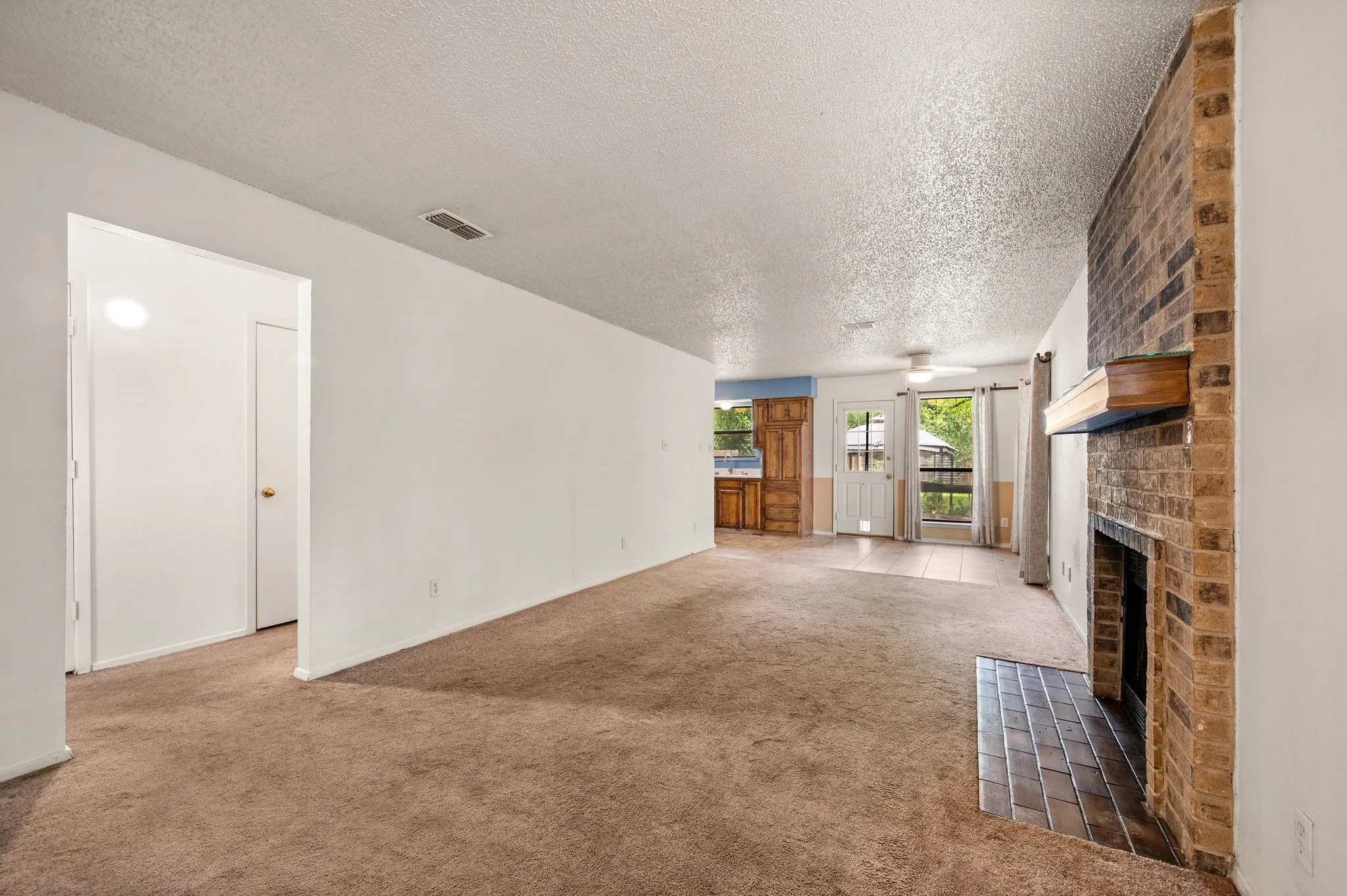Brick fireplace with wood mantel, brown carpet flooring, and white walls