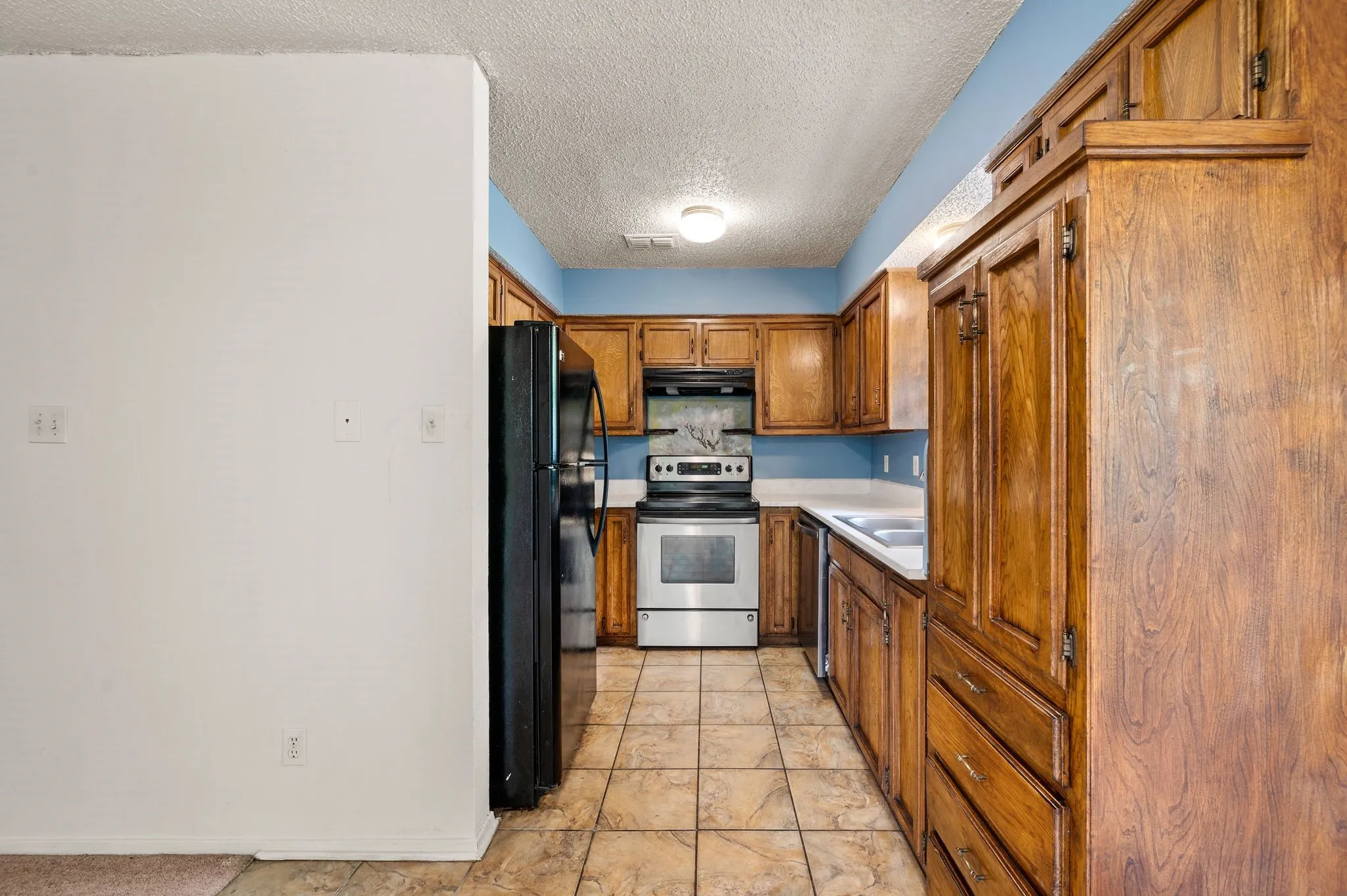 Kitchen featuring wood cabinetry, tile flooring, stainless steel range, and a dual basin sink
