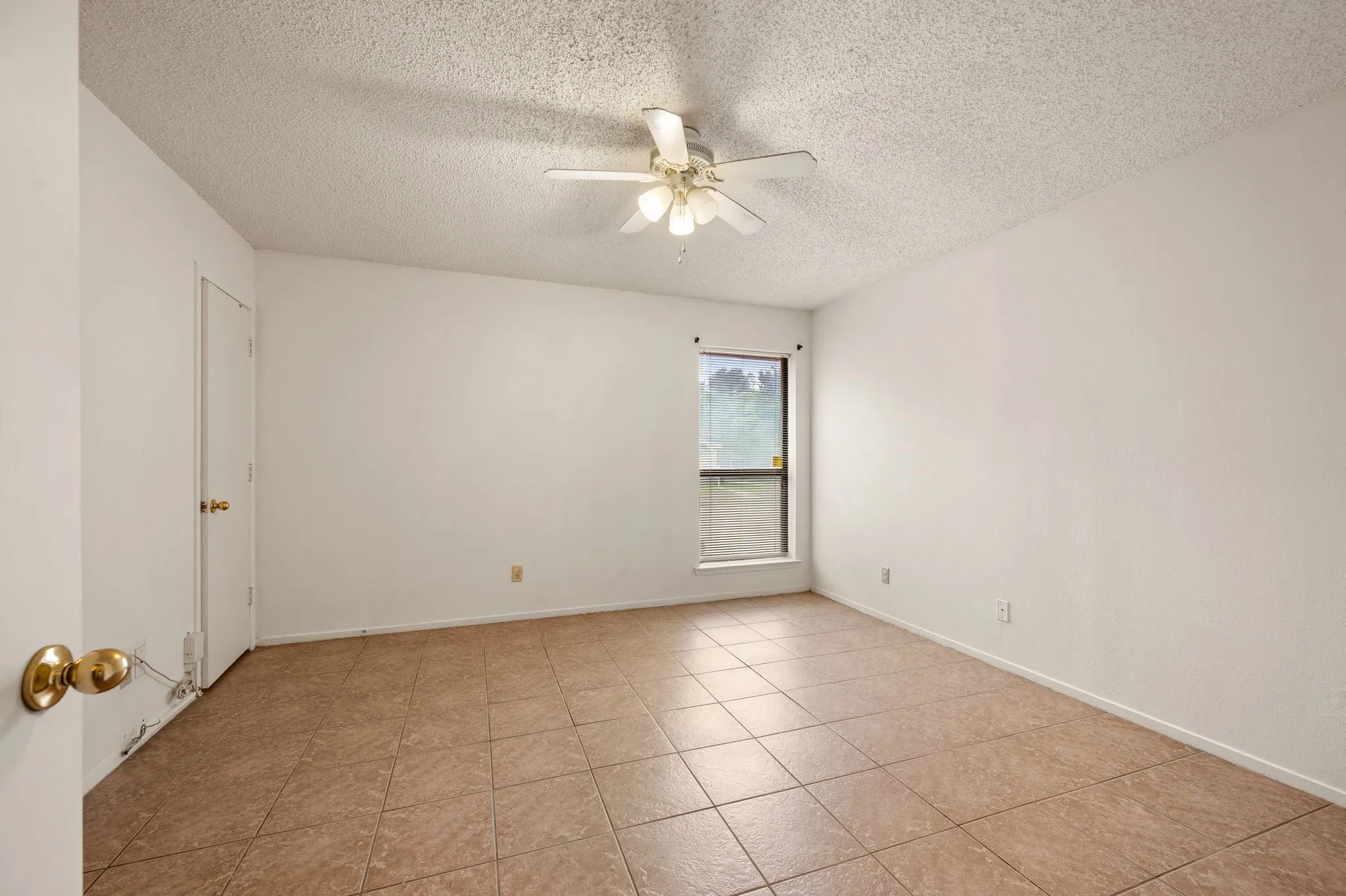 Neutral toned floor tiles, white walls, and a ceiling fan with integrated lighting