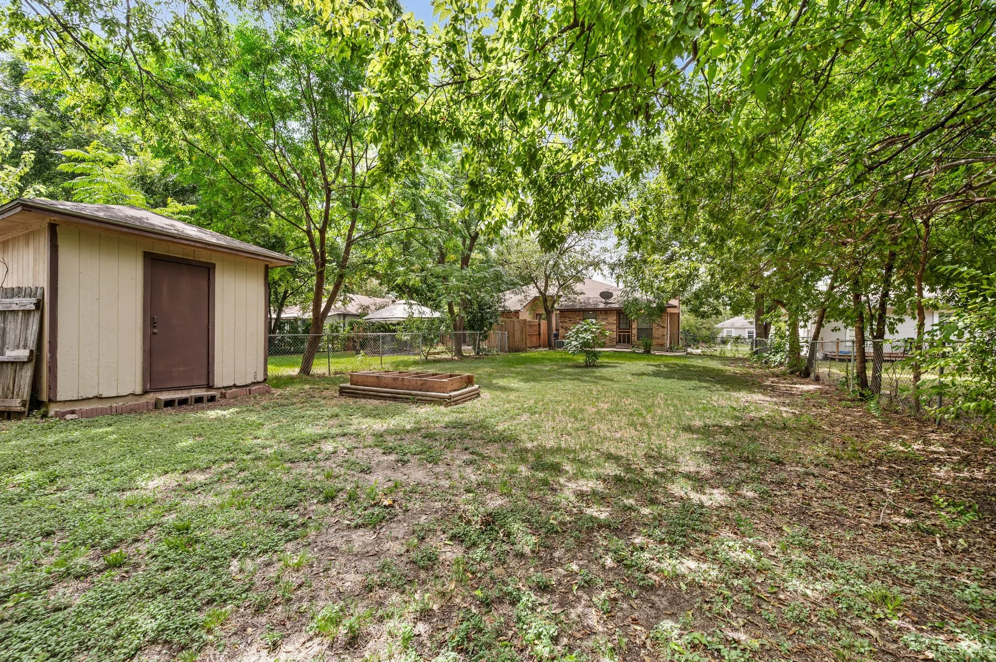  322 Expansive backyard featuring a storage shed, established trees, a raised garden bed, and a chain-link fence