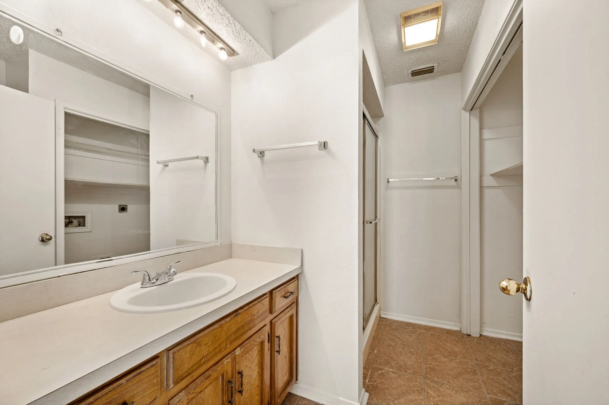 Bathroom featuring a wood-finish vanity with a white countertop and integrated sink, a large wall-mounted mirror, and a glass-enclosed shower