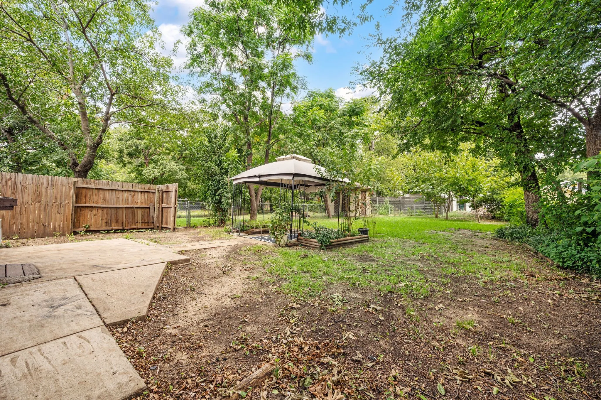 Expansive backyard featuring mature trees, a wooden privacy fence, a concrete patio, and a gazebo structure